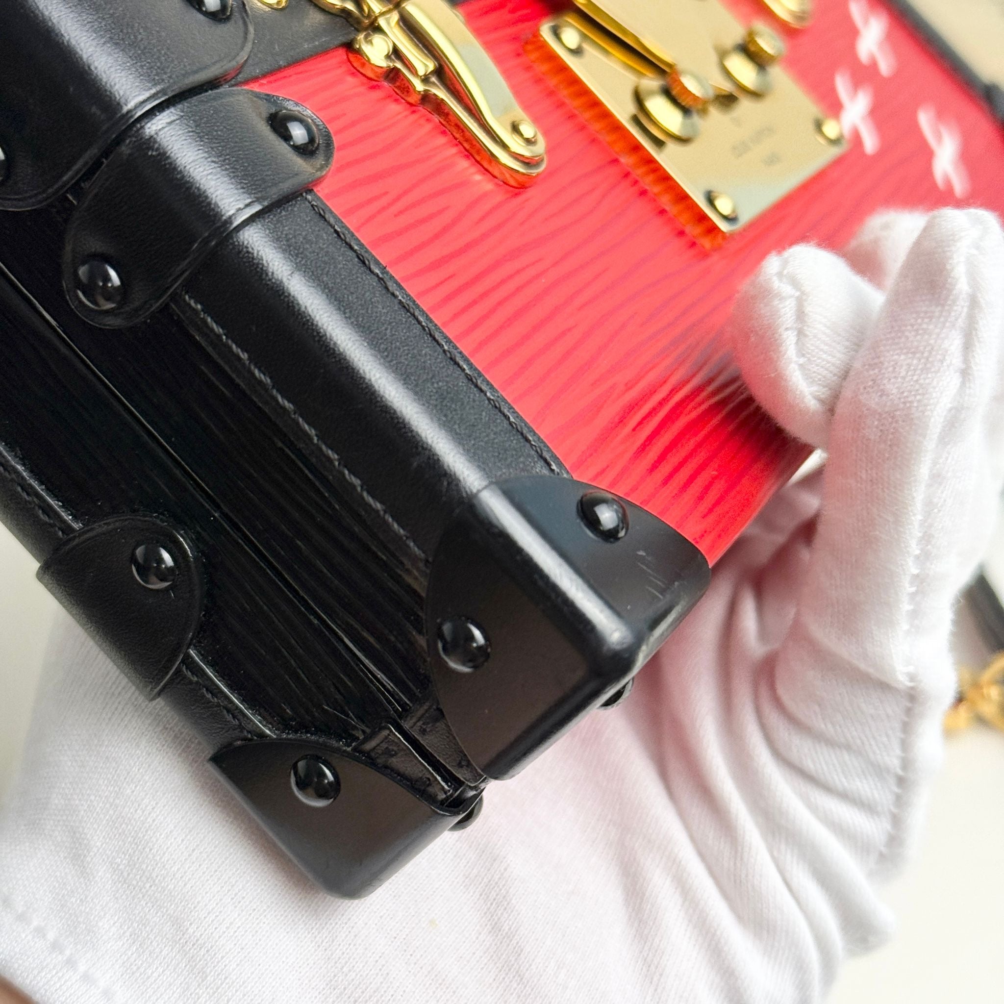Close-up of a red suitcase with black and gold accents, held by a gloved hand.