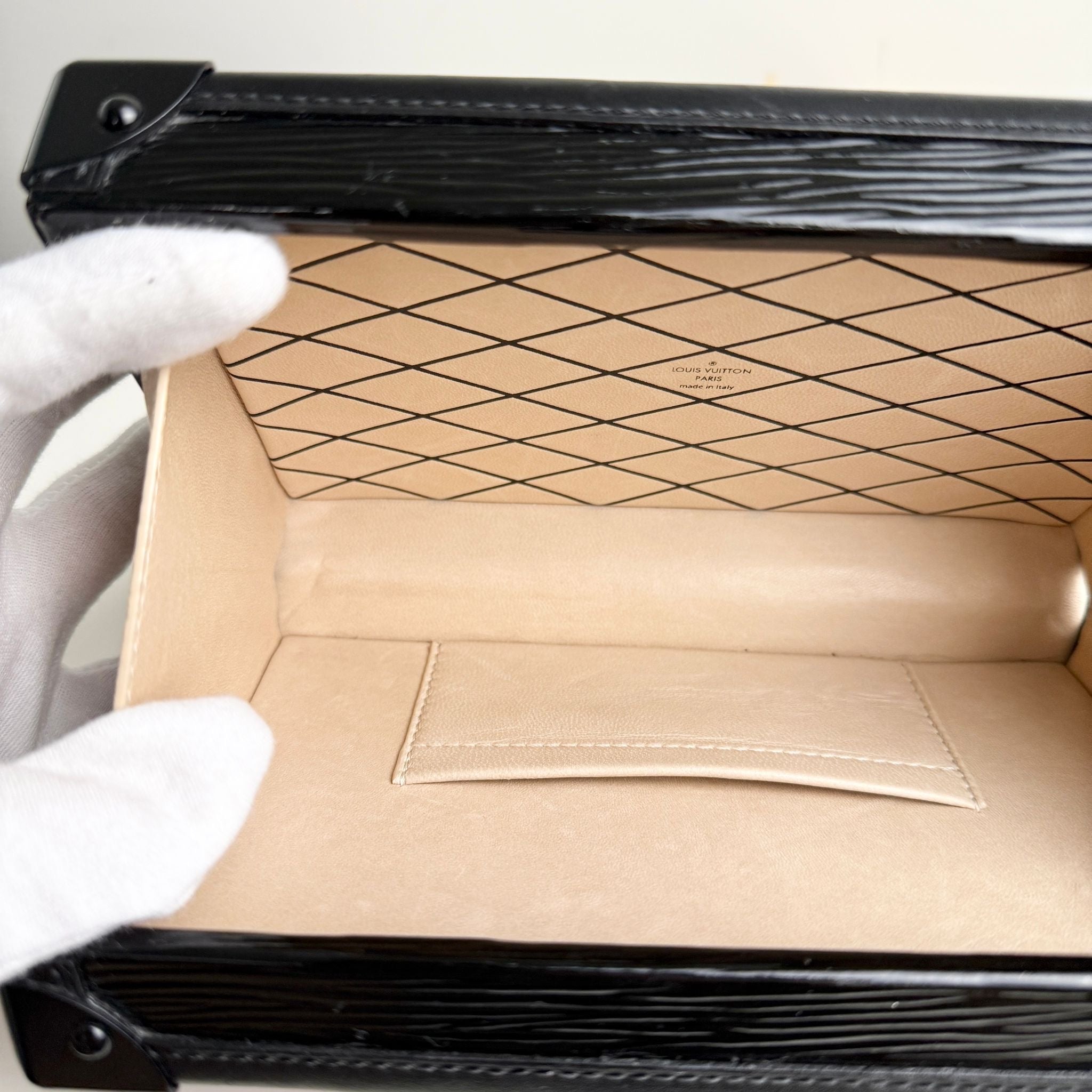 Close-up of a cardboard box with a black border and a white glove holding it.