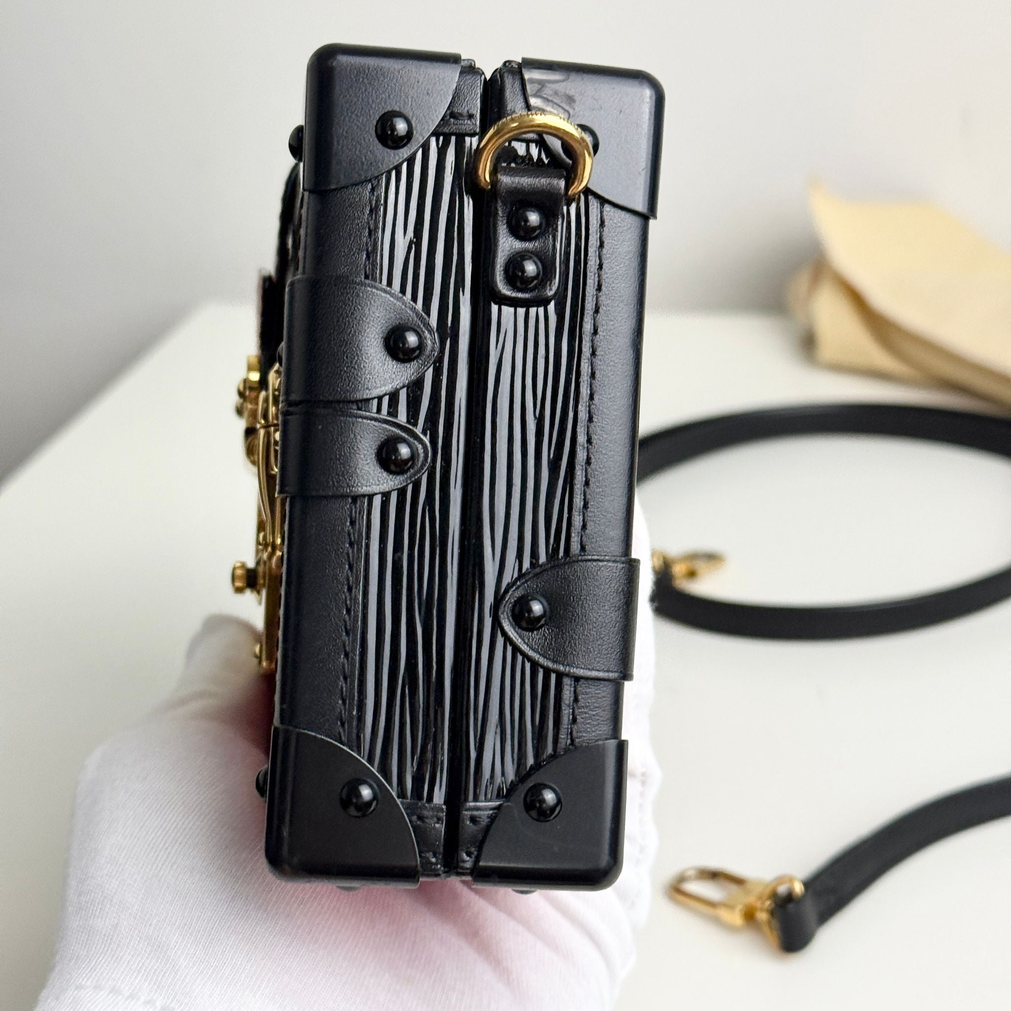 Black leather handbag with gold accents held by a person wearing a white glove.