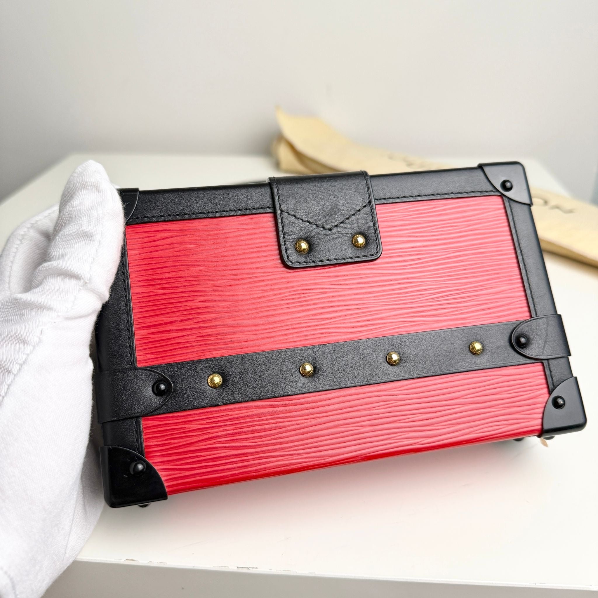 Red clutch bag with black strap and gold studs on a white surface