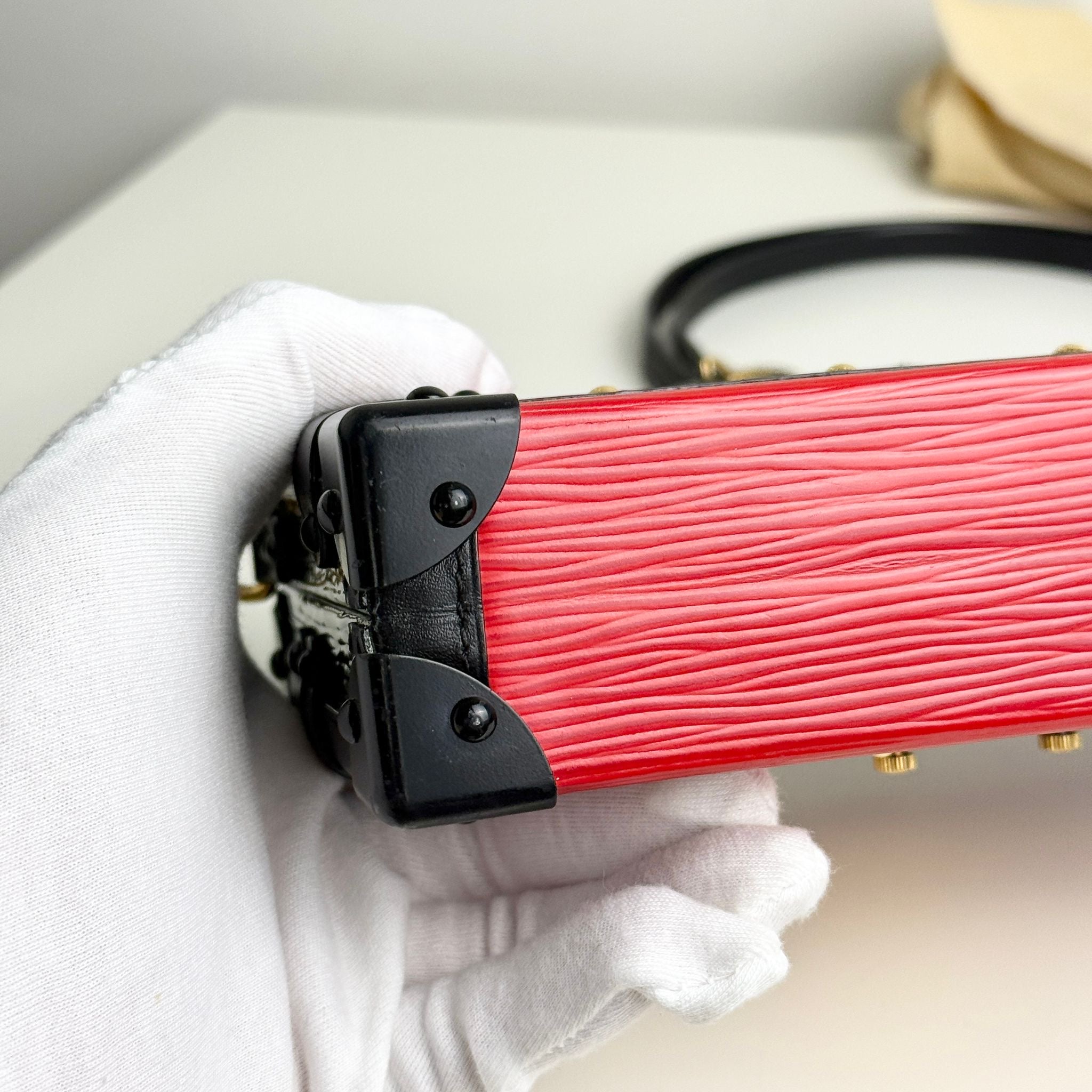 Red guitar case with black latches held by a gloved hand on a light background