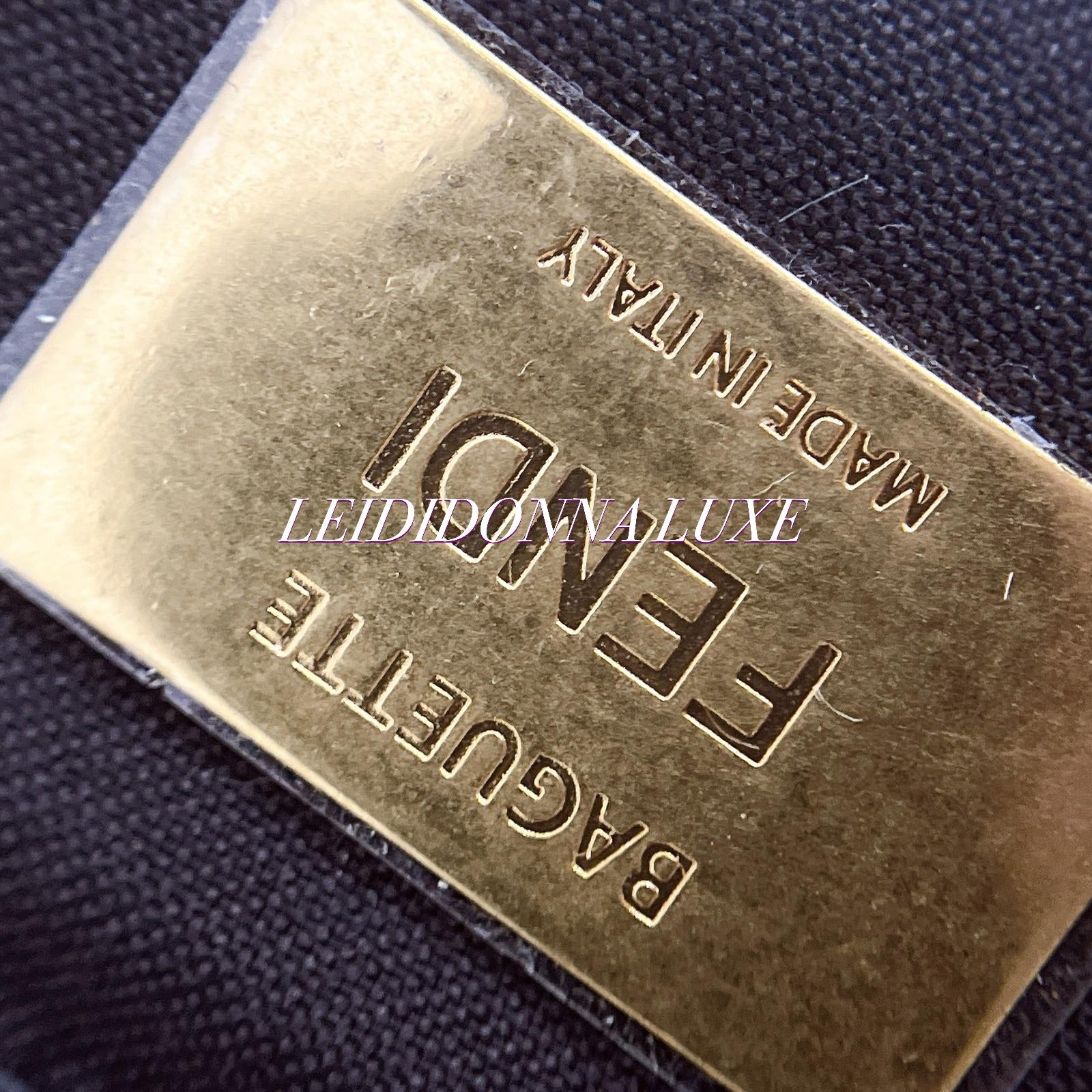 Close-up of a gold Fendi baguette bag label on black fabric background
