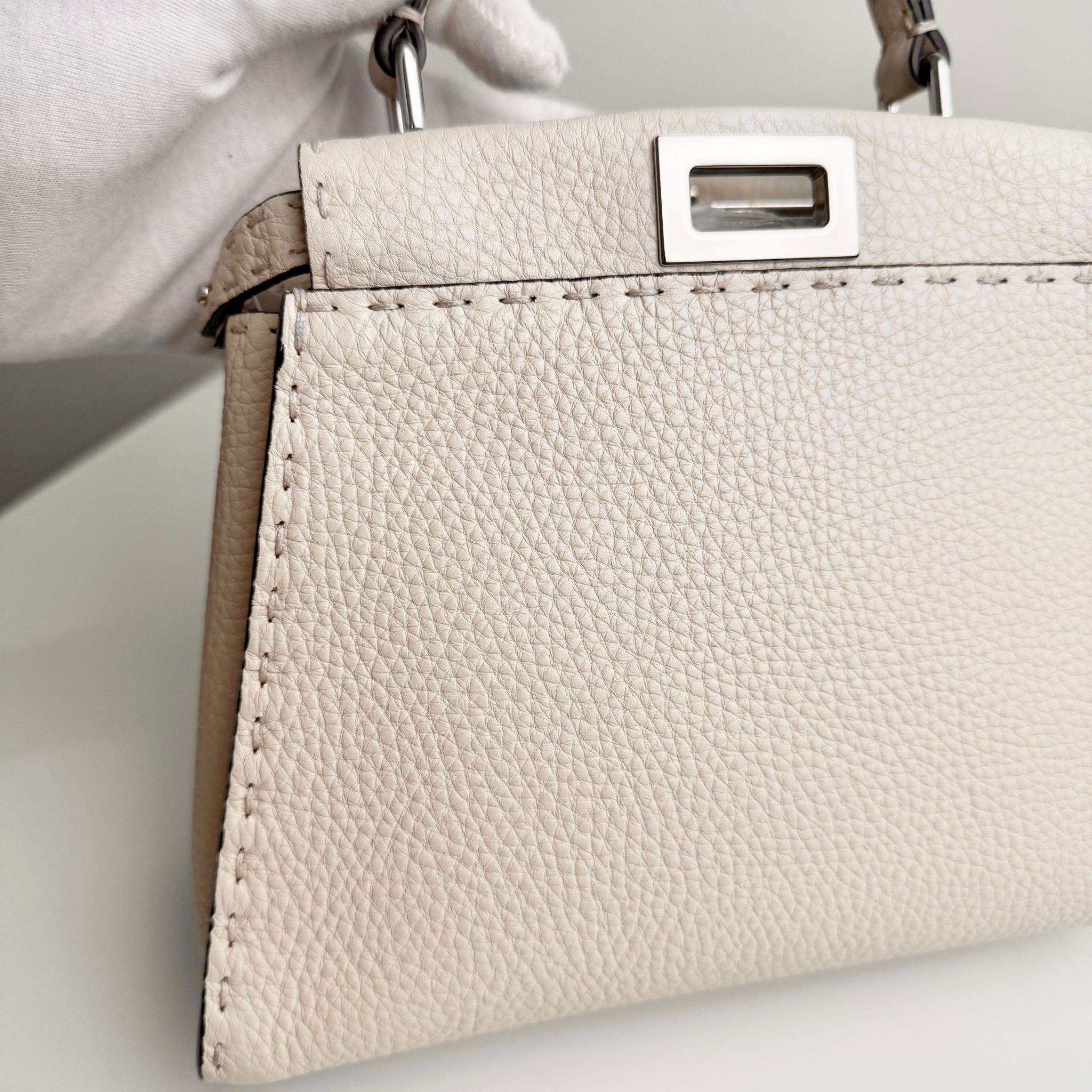 Beige handbag with a silver clasp on a light gray background