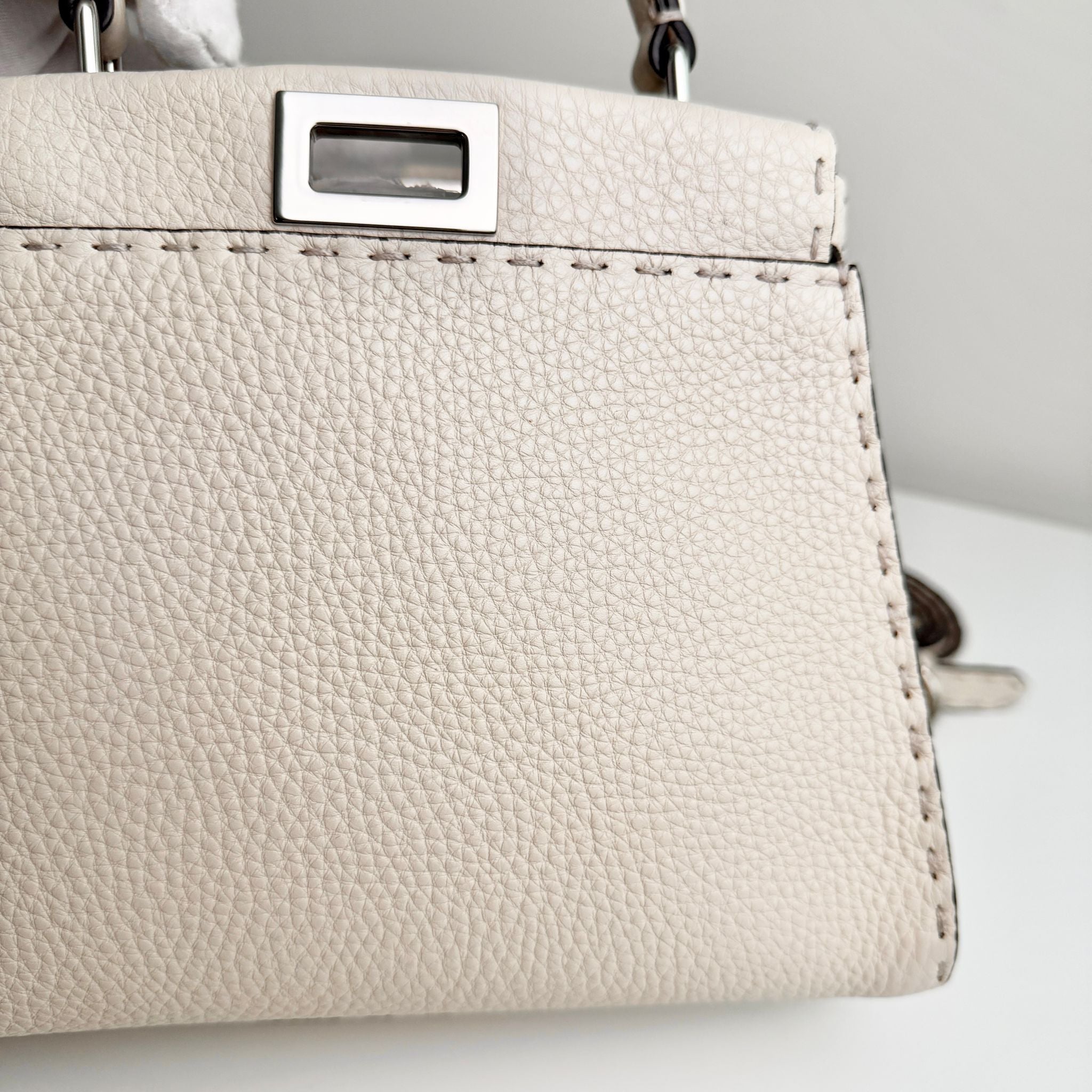 Close-up of a beige handbag with a silver clasp on a light background