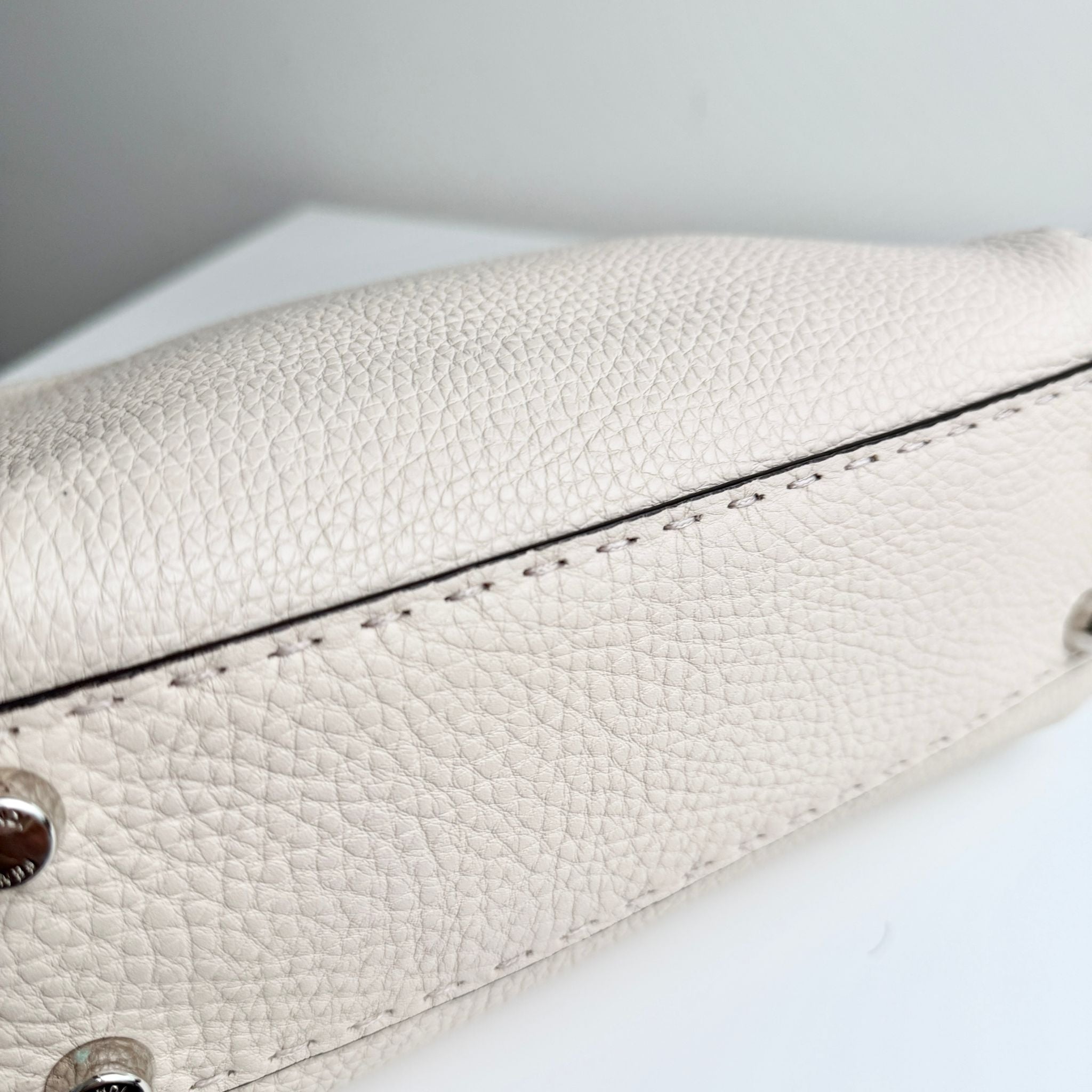 Close-up of a white leather handbag with visible stitching on a light background