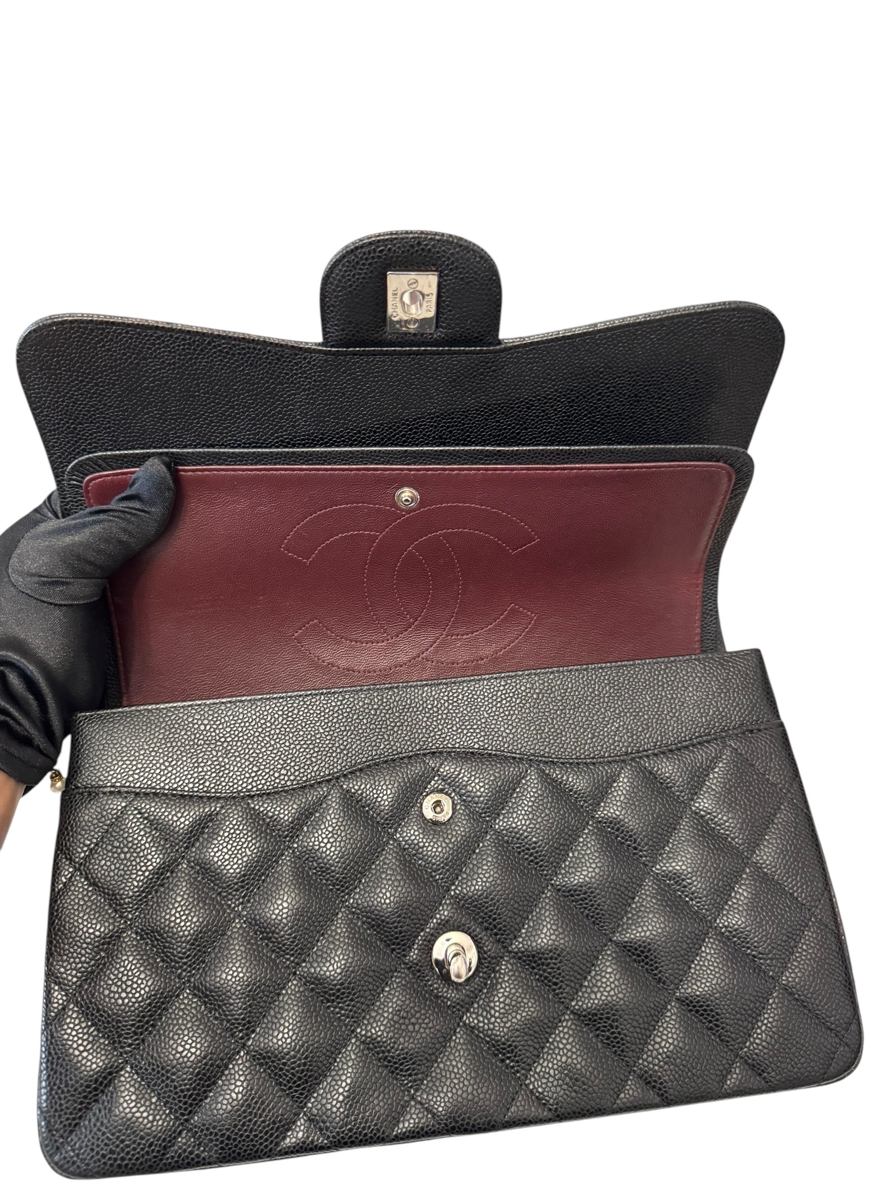 Black quilted handbag with red interior and gold hardware, held open by a gloved hand.