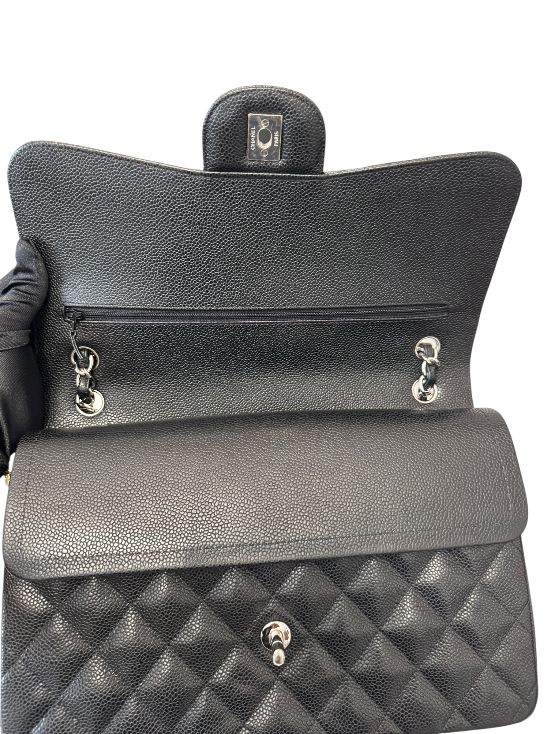 Black quilted handbag held by a gloved hand on a white background