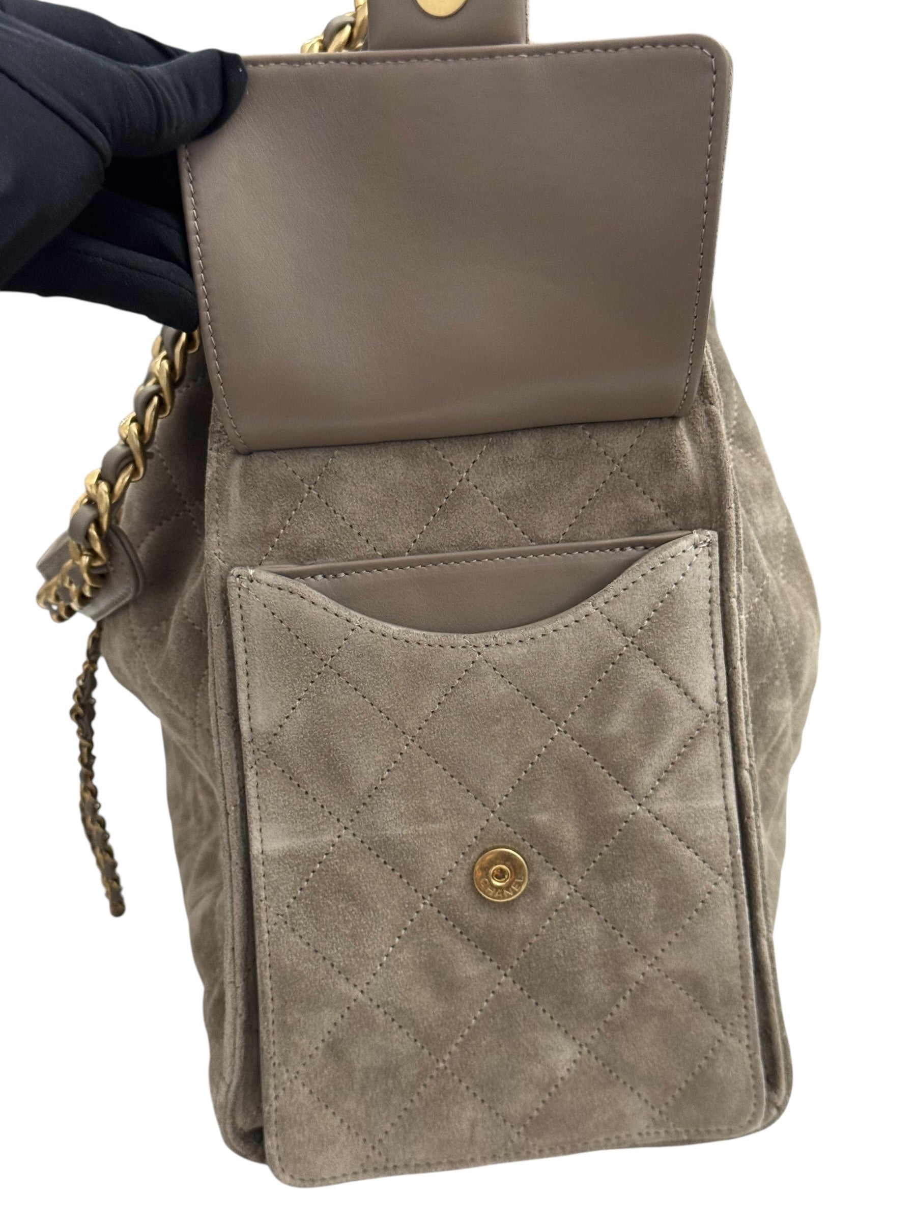 Gray quilted handbag with gold accents held by a gloved hand on a white background