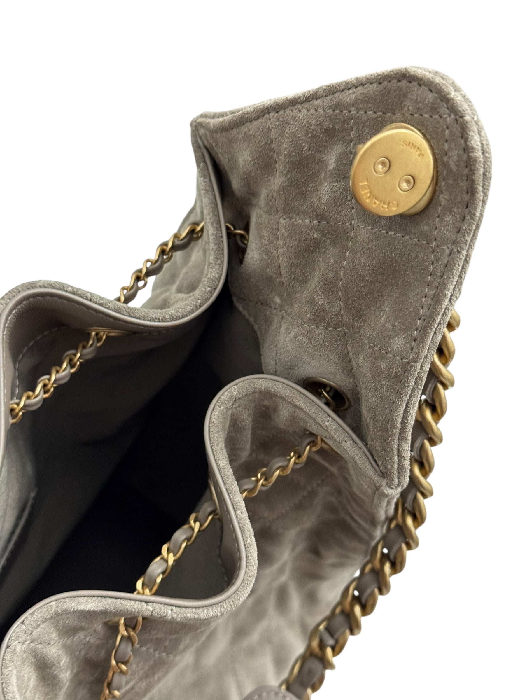 Gray suede handbag with gold chain and button detail on a white background