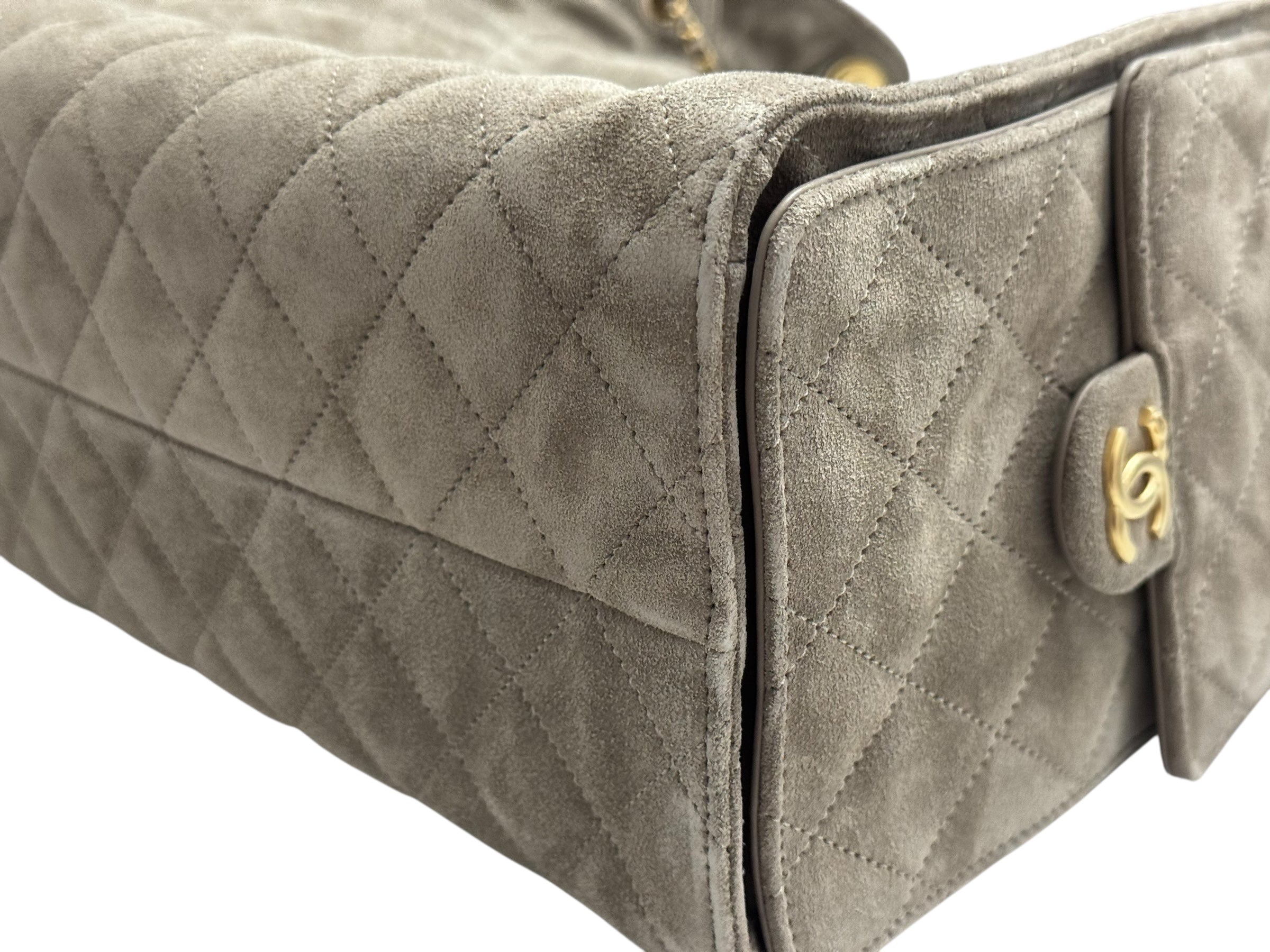 Close-up of a quilted gray handbag with a gold logo on a white background