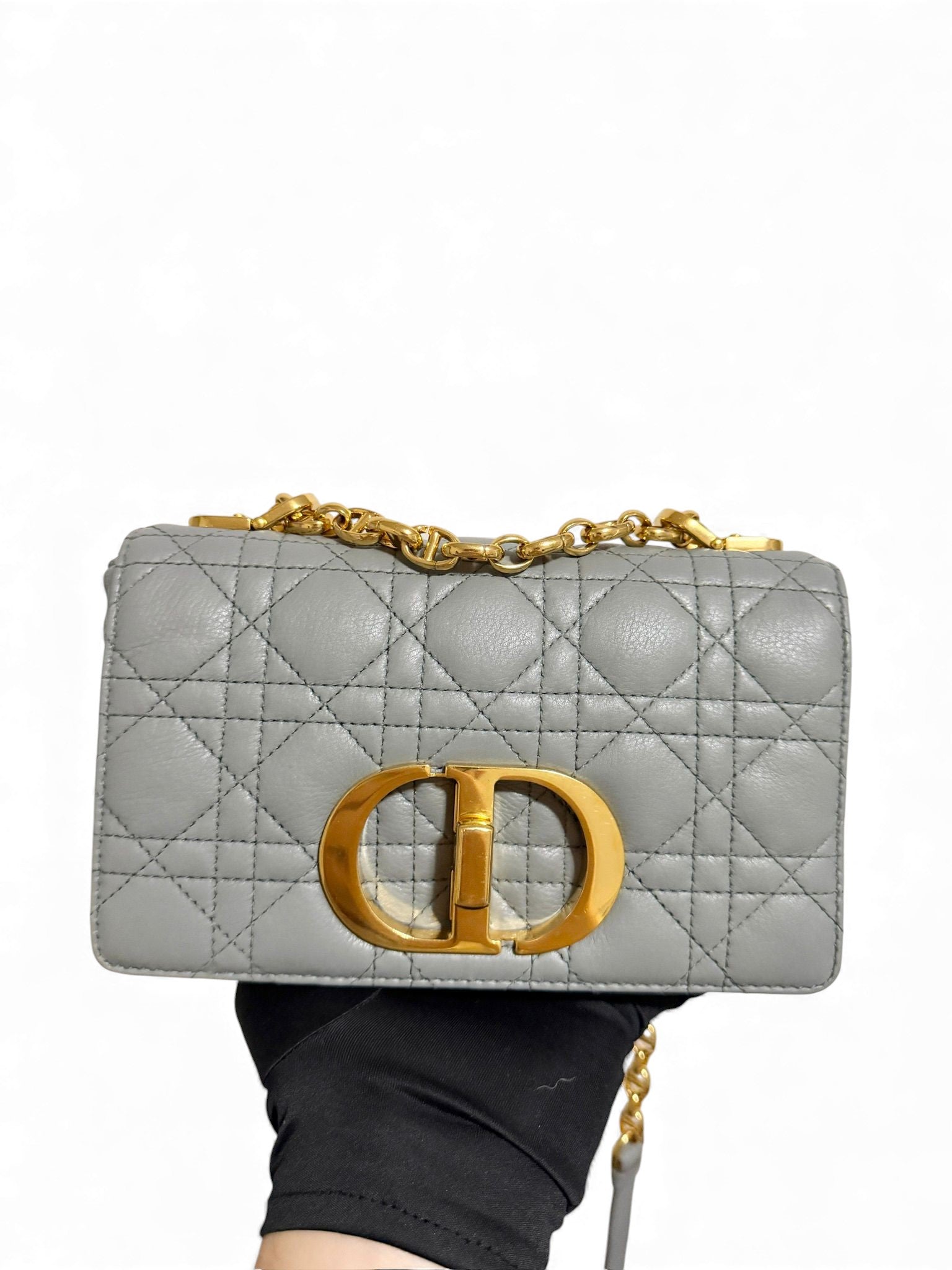 Gray quilted handbag with gold chain and clasp held by a hand against a white background