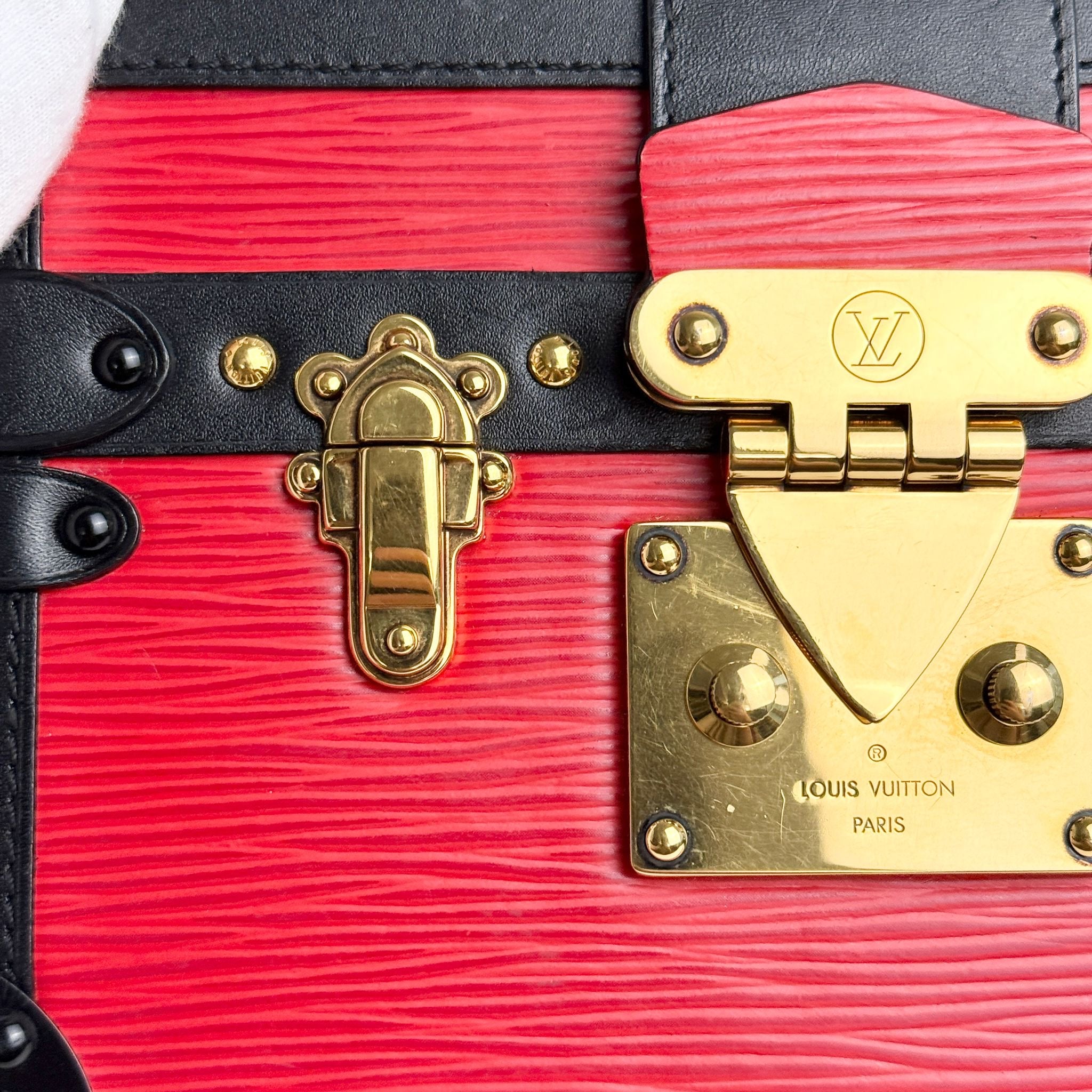 Close-up of a red and black Louis Vuitton handbag with gold hardware.