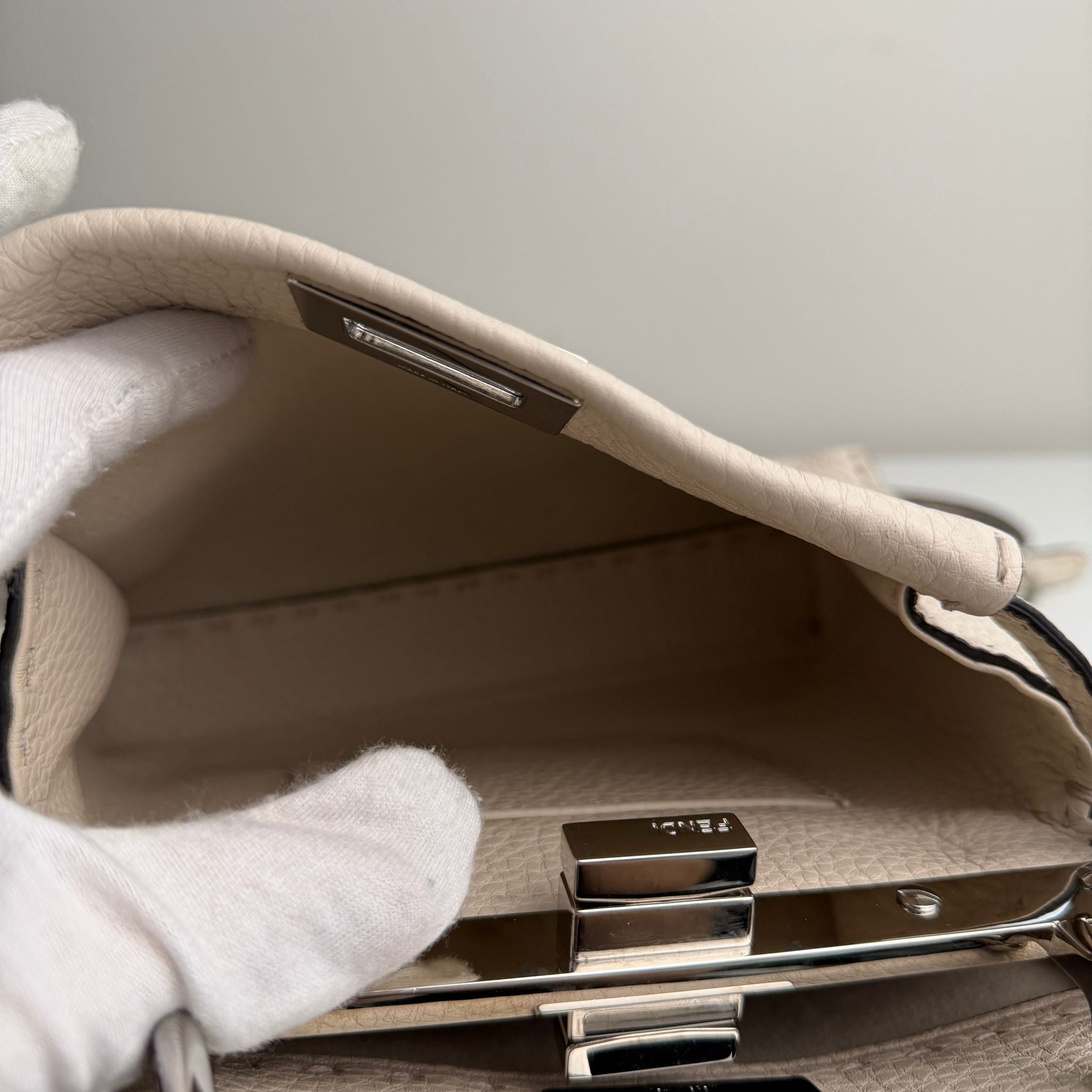 Close-up of a beige handbag with a metallic clasp on a light gray background