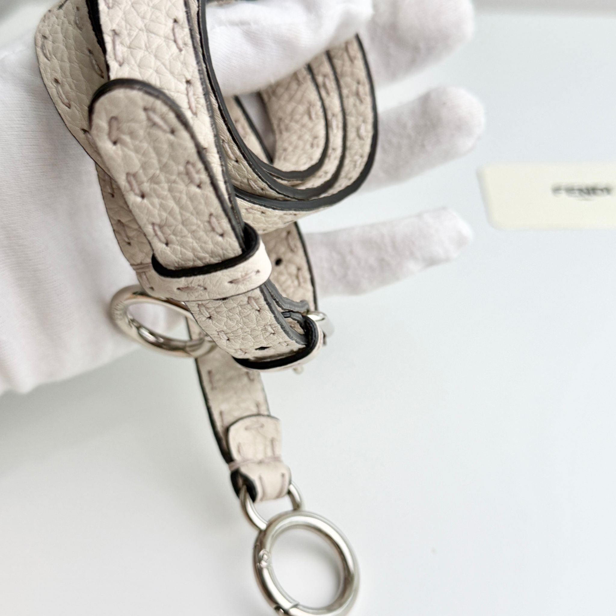 Close-up of a beige leather strap with metal hardware on a white background