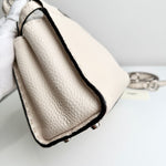 将图片加载到图库查看器，Close-up of a beige handbag with black trim held by a gloved hand on a light gray background.
