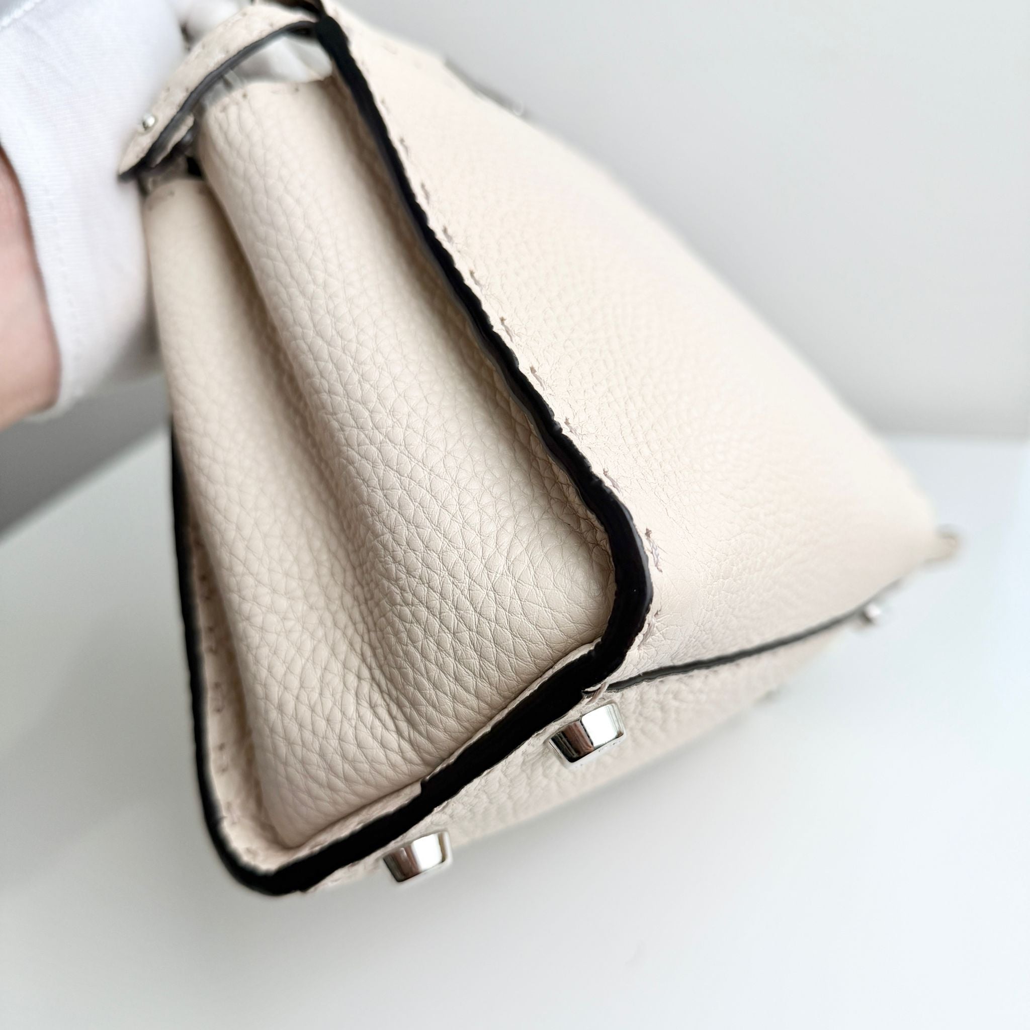 Close-up of a beige leather handbag with a black trim on a light background
