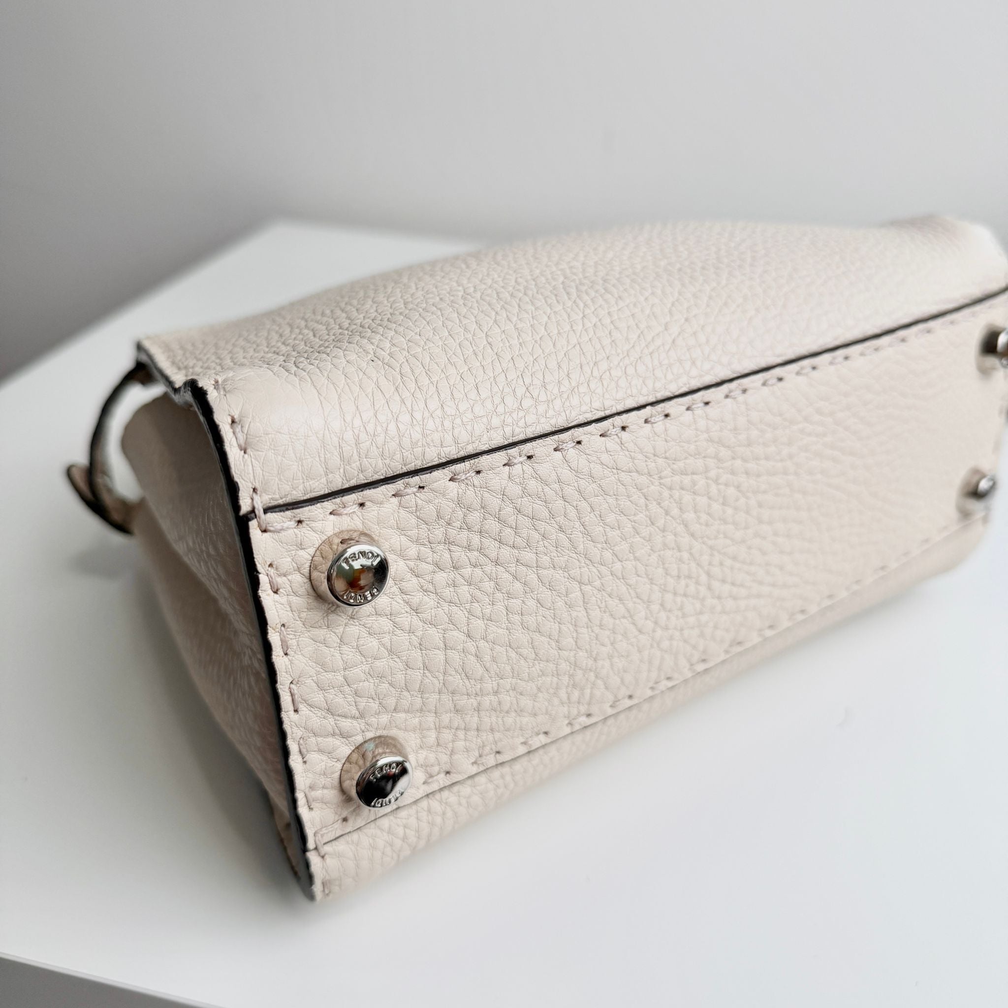 Beige leather clutch bag with silver accents on a white surface