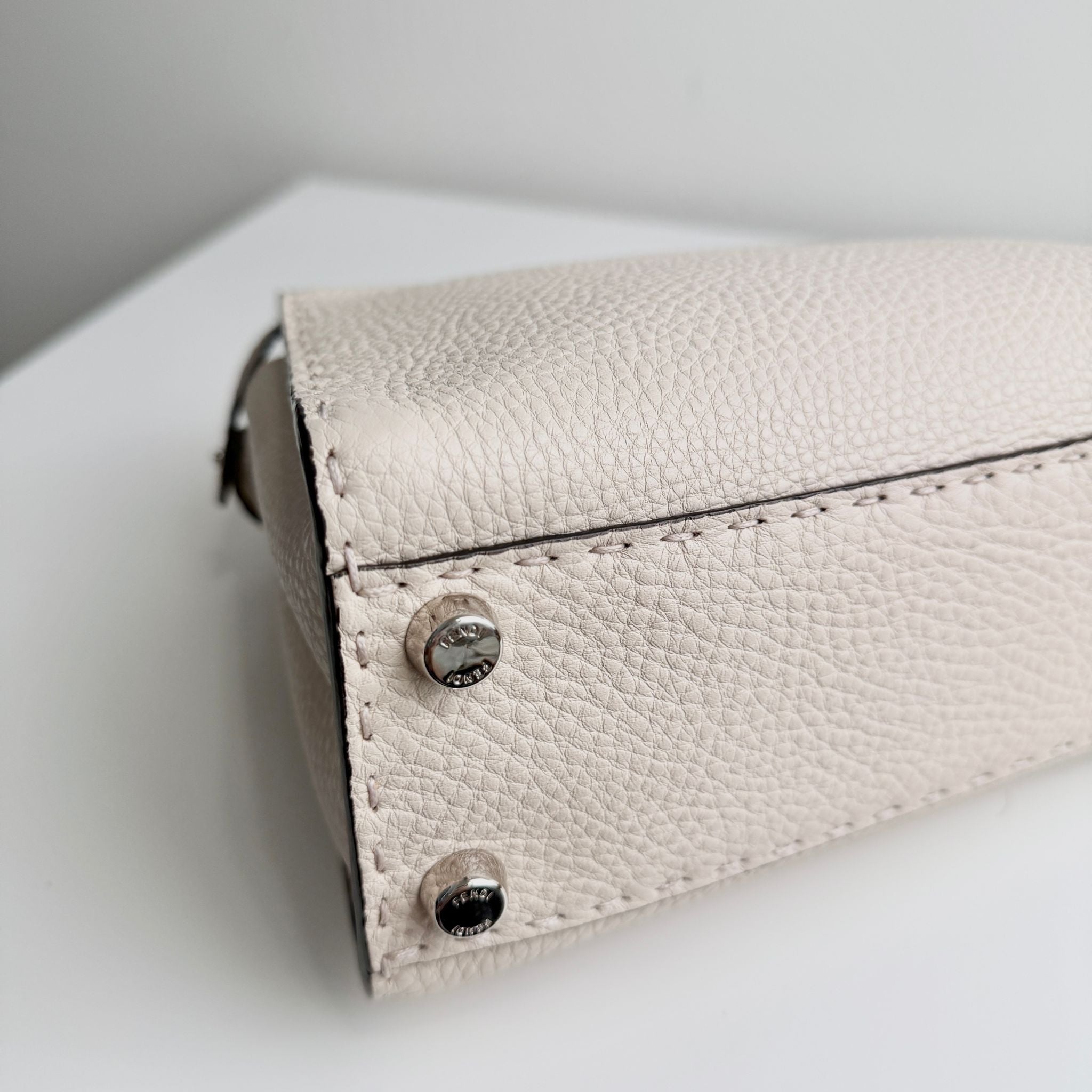 Close-up of a light-colored leather wallet with metal buttons on a white surface.