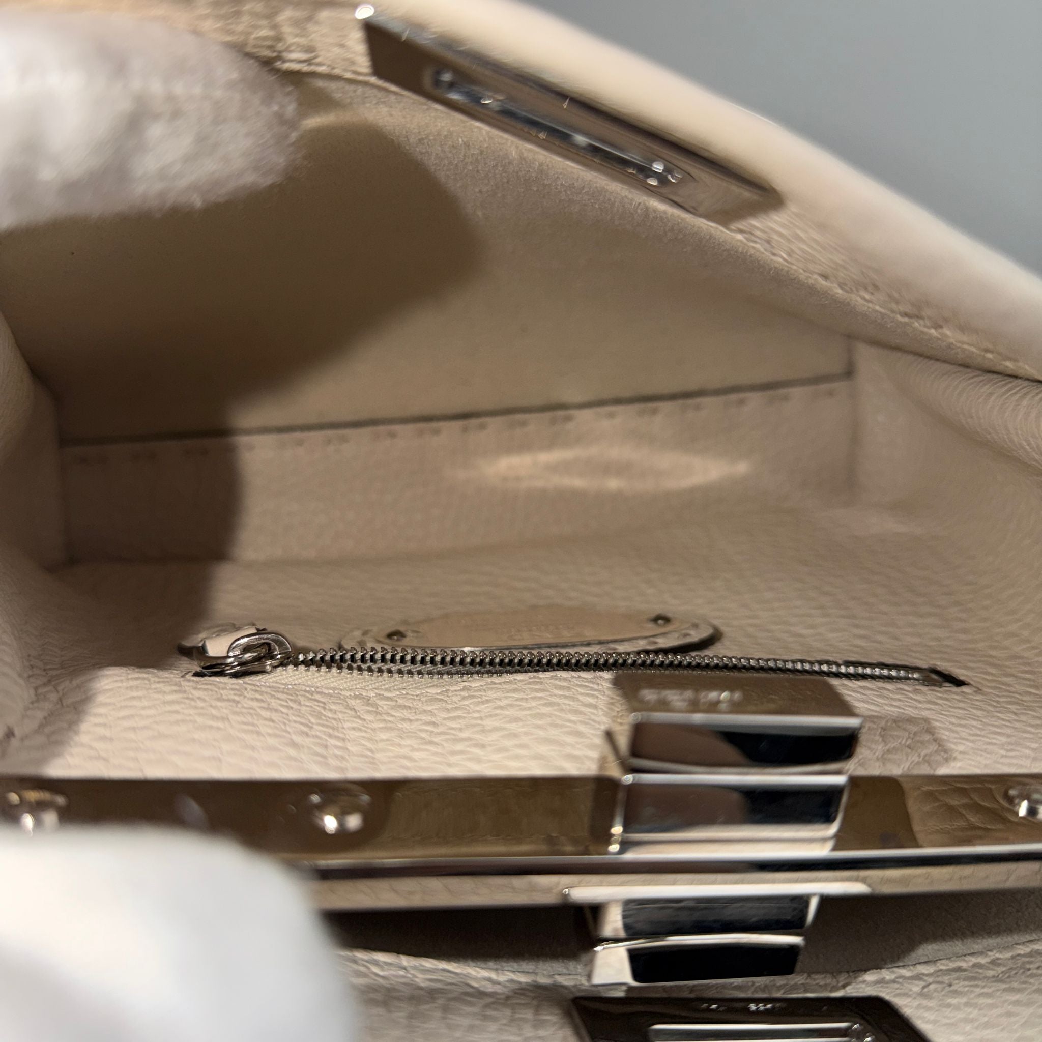 Close-up of a beige handbag with a metallic clasp and zipper.