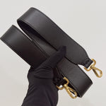 将图片加载到图库查看器，Black leather bag strap with gold hardware held by a gloved hand on a light gray background

