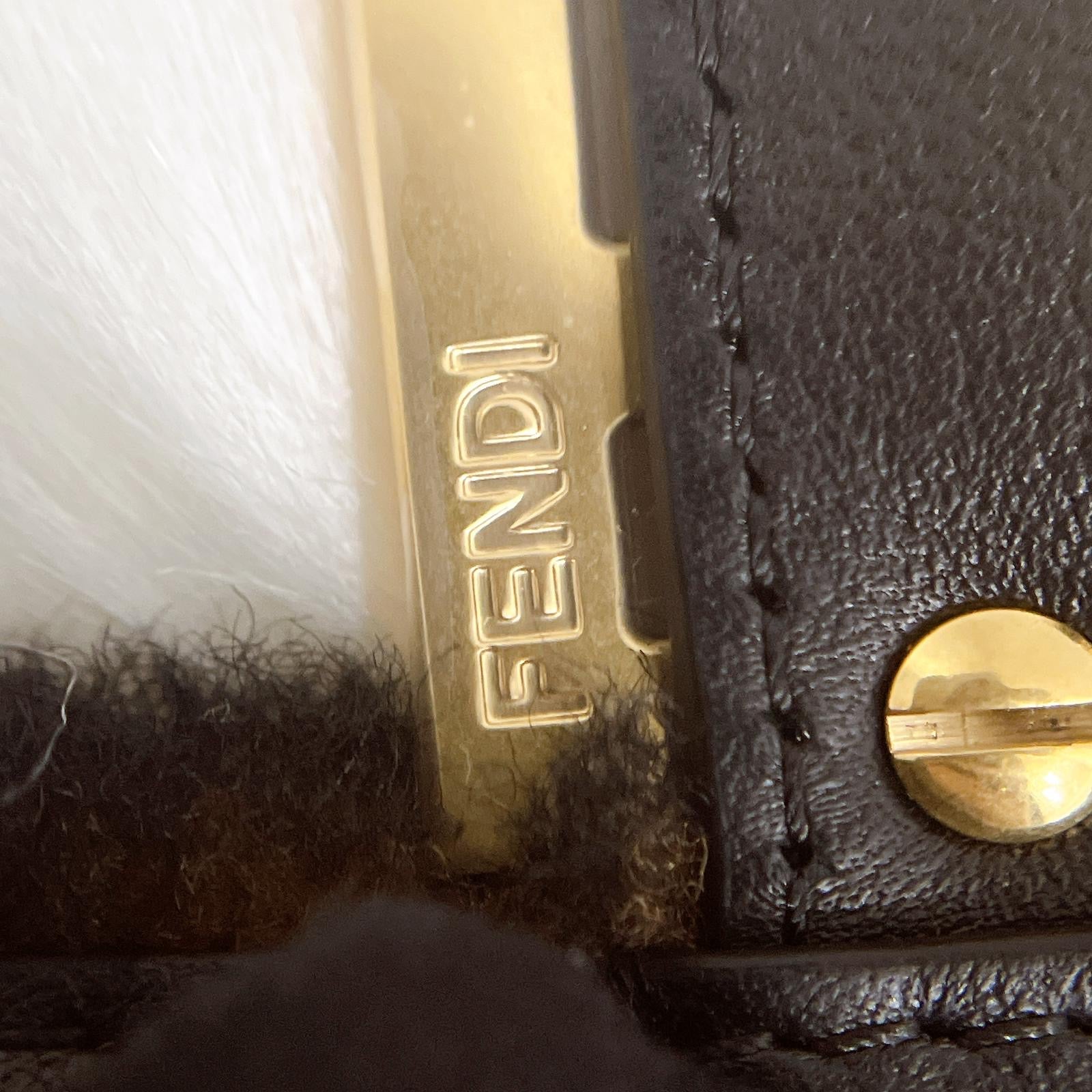 Close-up of a Fendi logo on a black leather product with gold hardware.