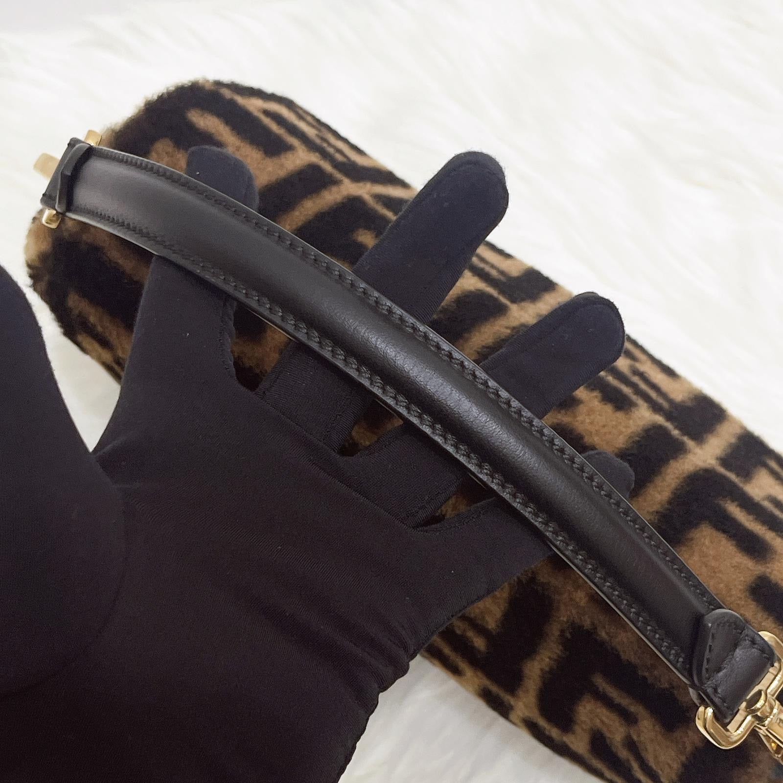 Black glove holding a black leather strap with a leopard print bag in the background
