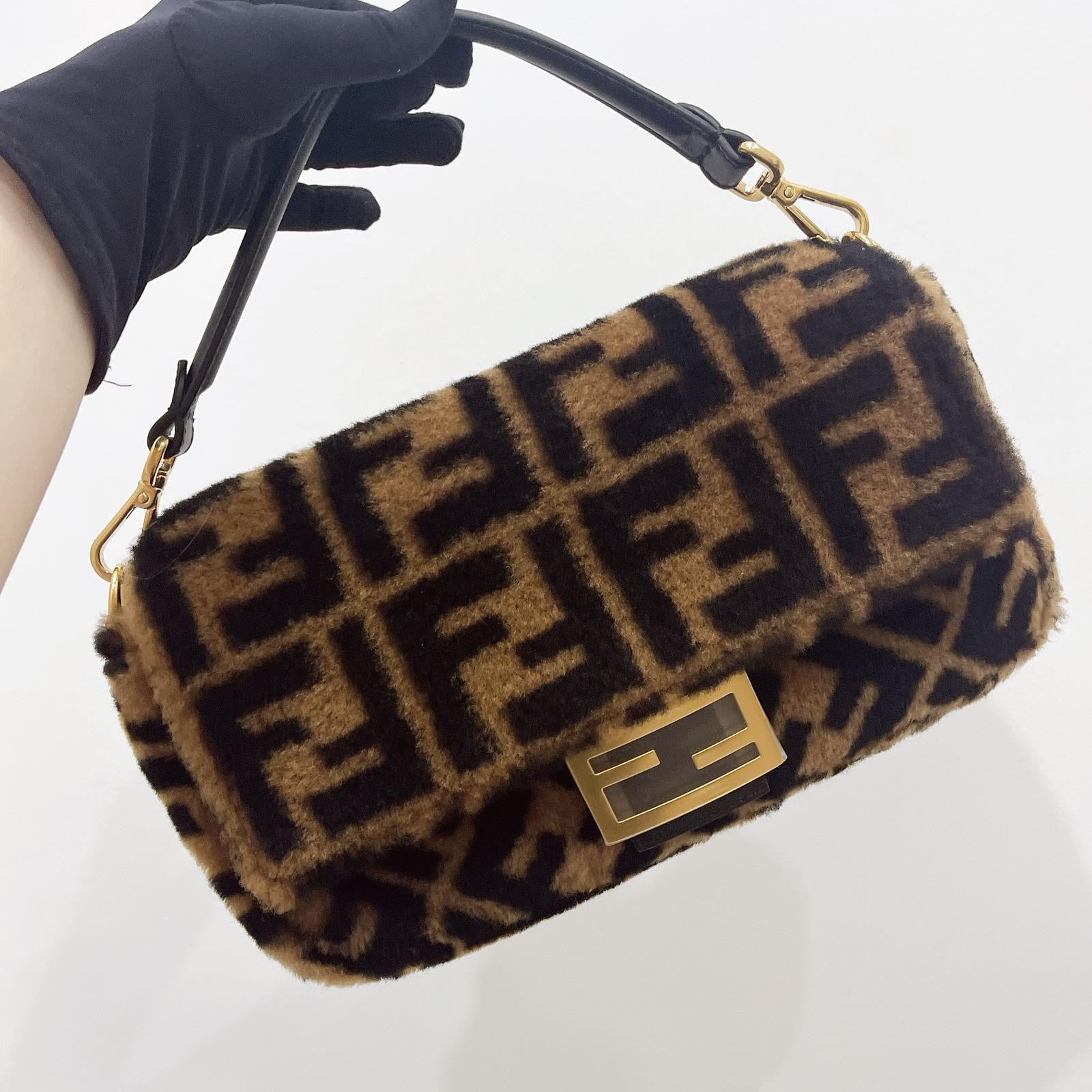 Fur-patterned handbag with gold accents held by a gloved hand on a white background