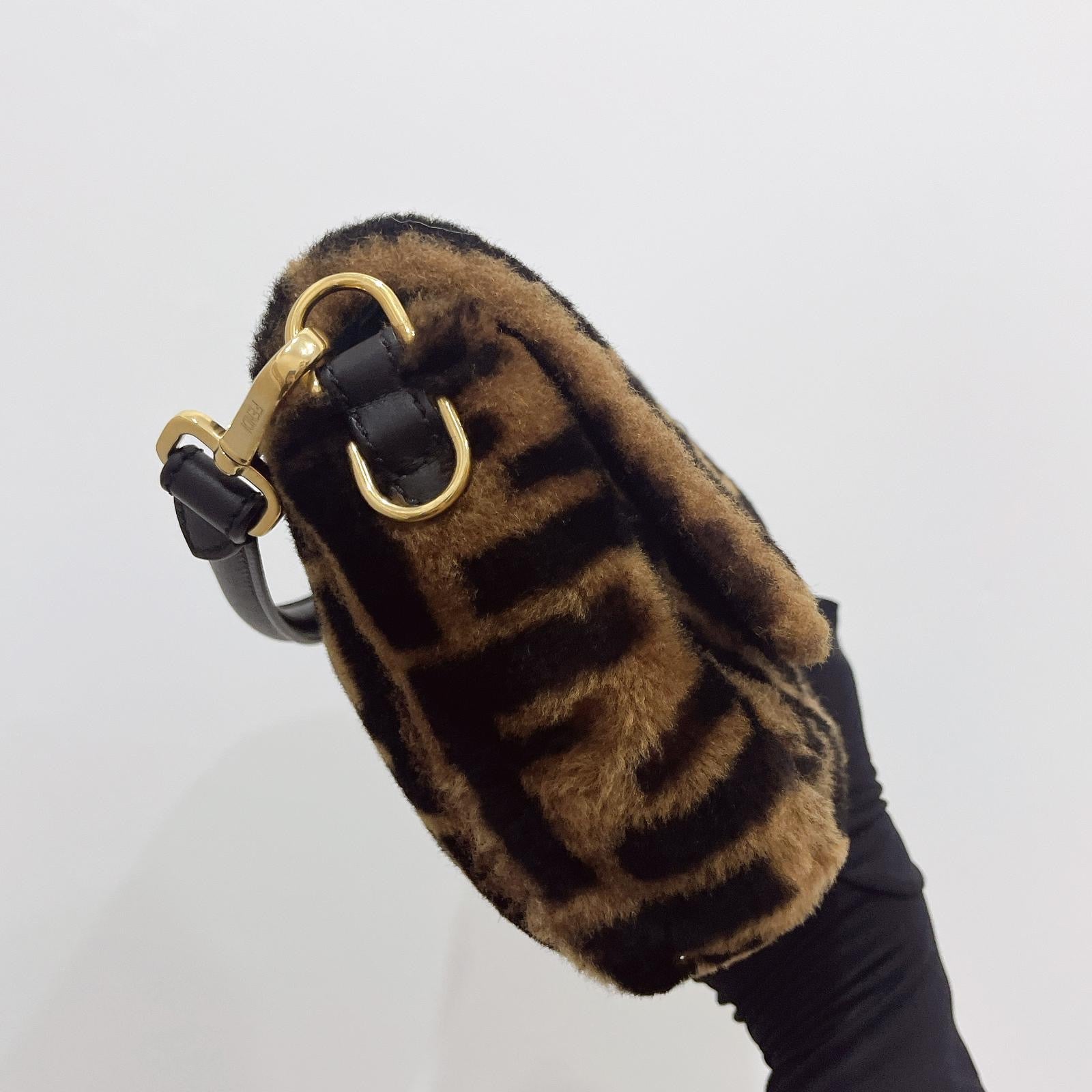 Brown fur pouch with gold clasp held by a gloved hand on a light gray background