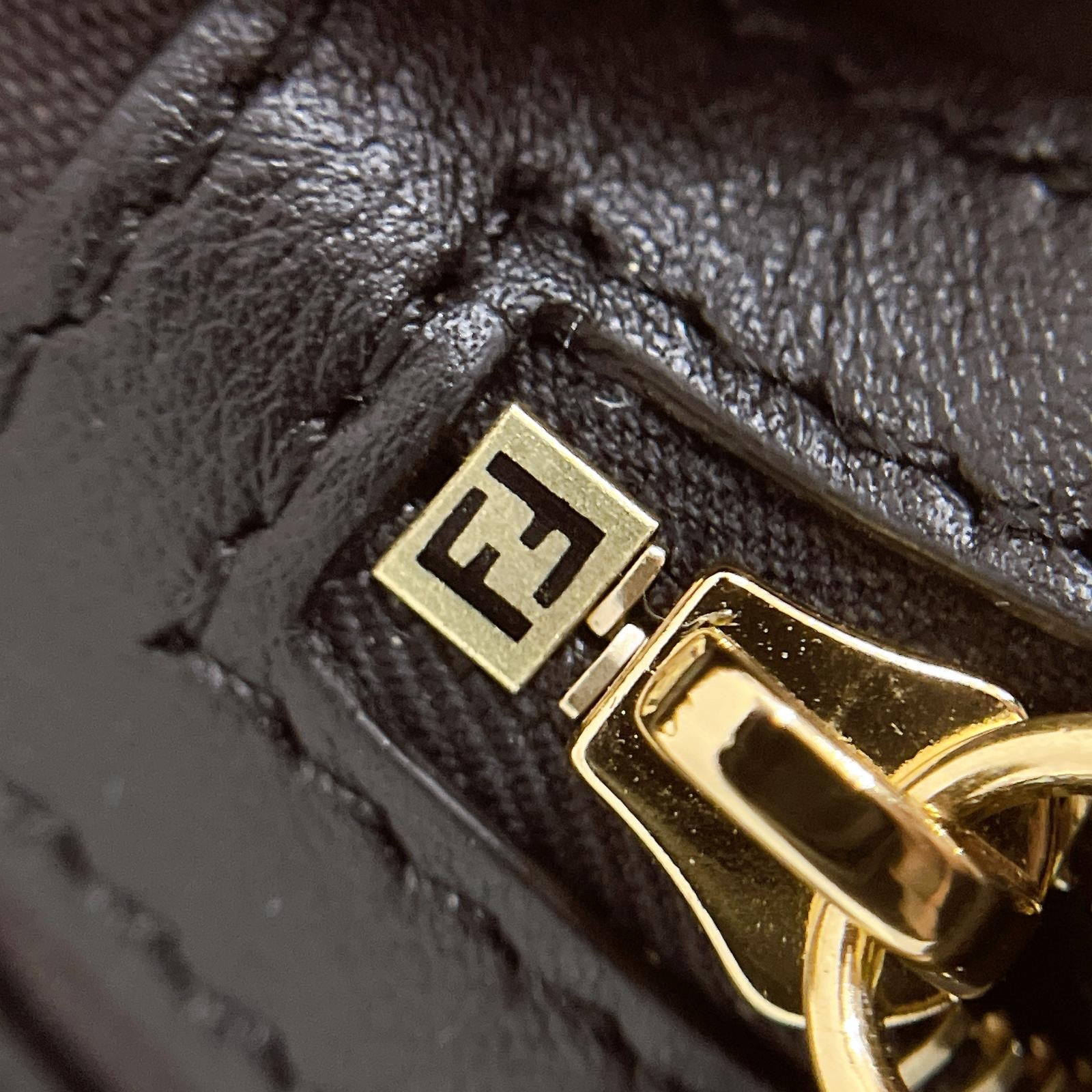 Close-up of a black leather bag with a gold clasp and logo.