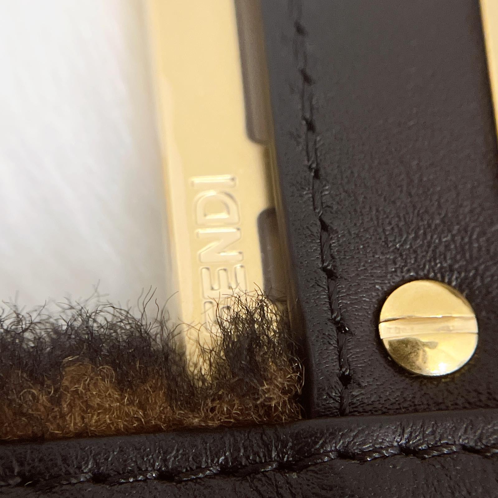 Close-up of a black leather product with gold hardware and 'Fendi' branding.