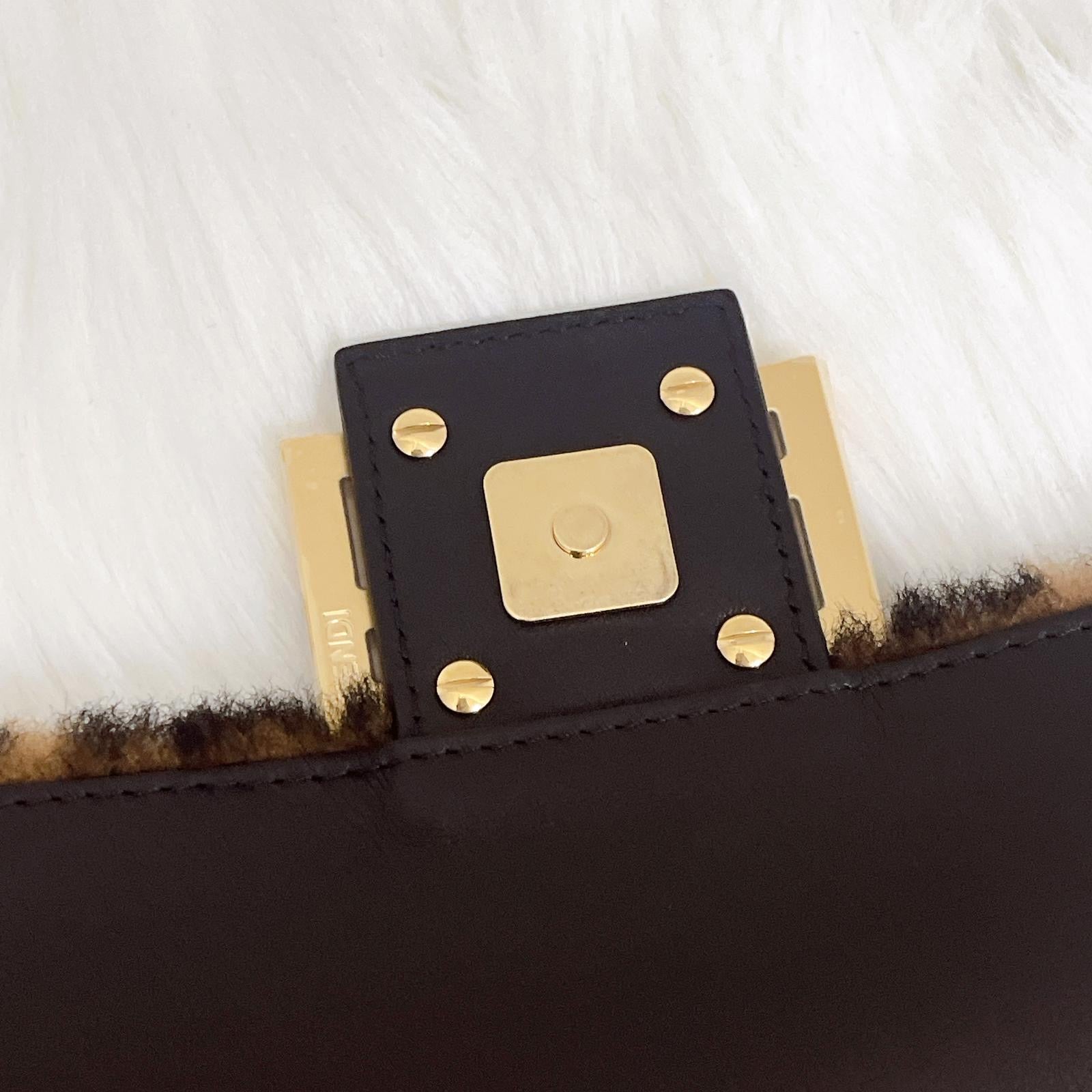 Close-up of a black leather clutch with gold hardware on a white fur background