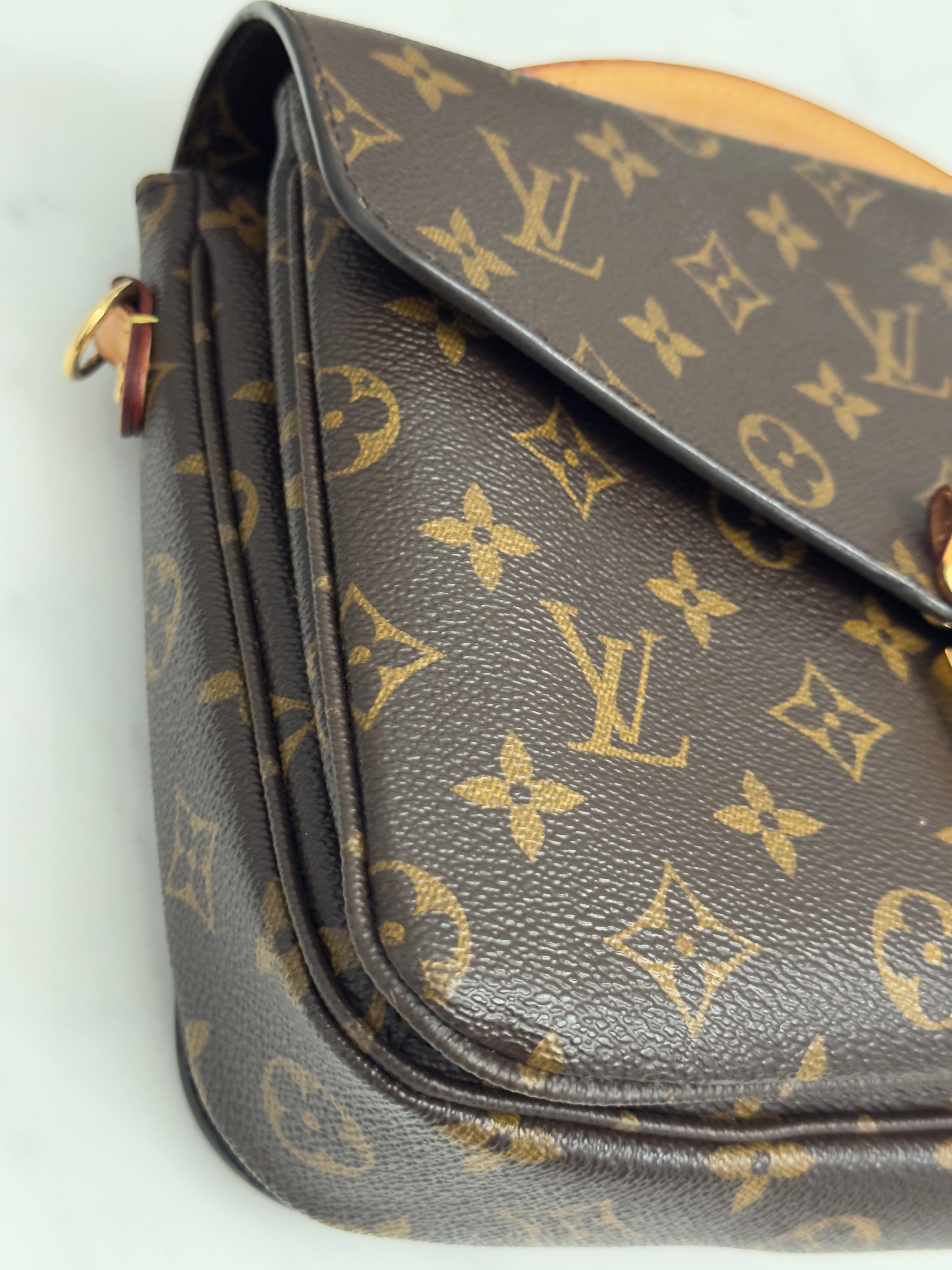 Brown leather handbag with gold monogram pattern on a white background