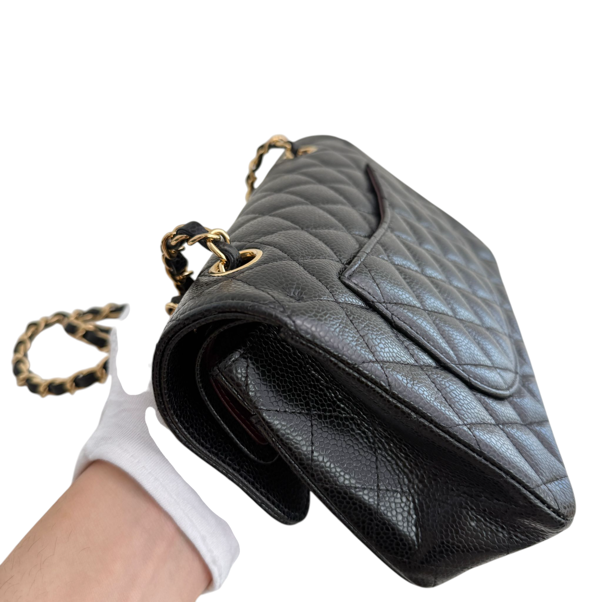Black quilted handbag with gold chain strap held by a gloved hand on a white background