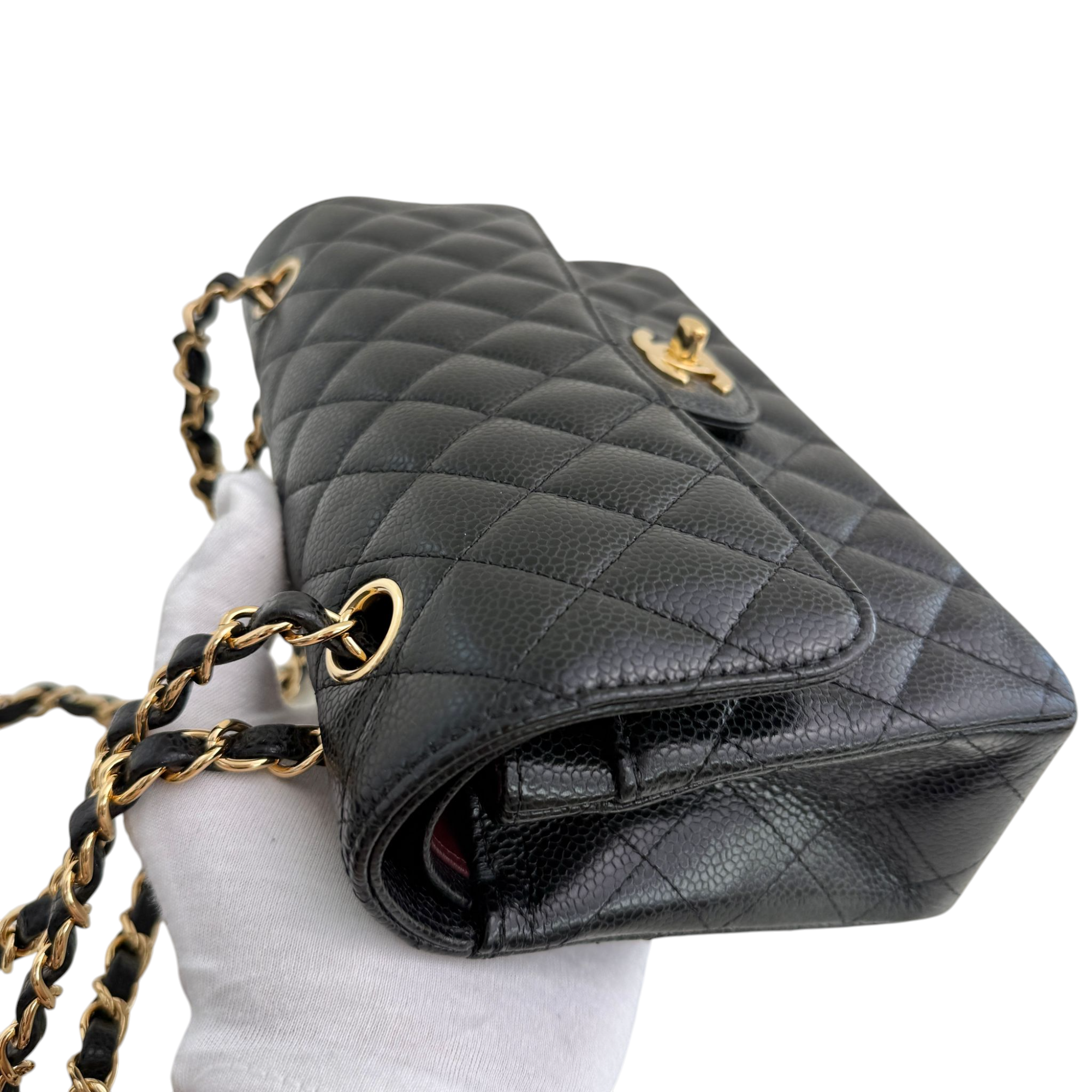 Black quilted handbag with gold chain strap on a white background