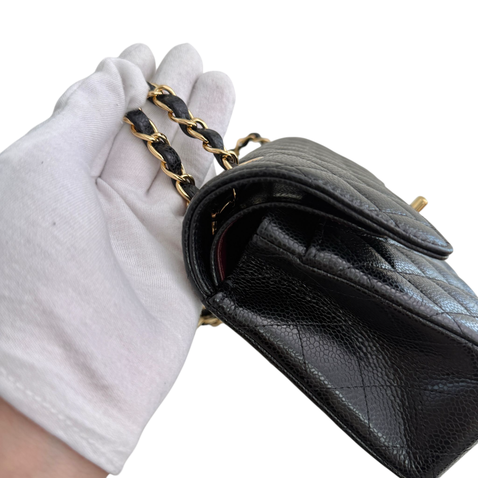 Black quilted handbag with gold chain strap held by a gloved hand on a white background