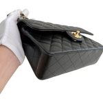 Charger l&#39;image dans la galerie, Black quilted handbag held by a gloved hand on a white background
