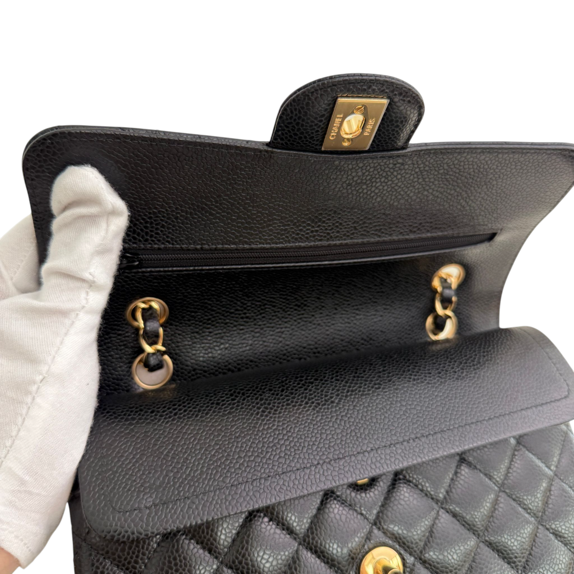Close-up of a black quilted handbag with gold hardware, held by a gloved hand.