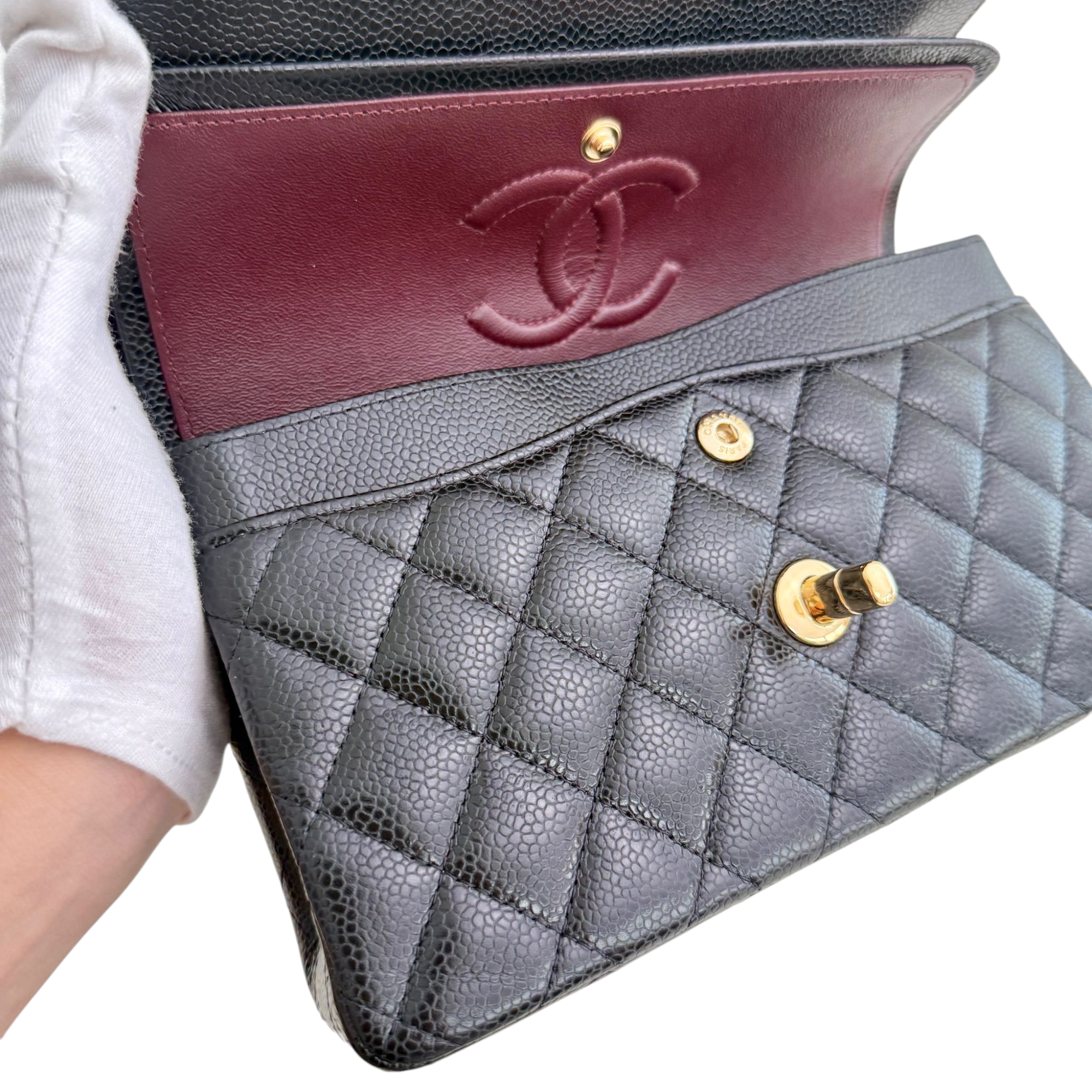 Chanel handbag with quilted design and red flap held by a gloved hand.