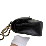 Charger l&#39;image dans la galerie, Black leather handbag with gold chain strap held by a gloved hand on a white background
