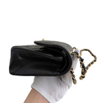 Charger l&#39;image dans la galerie, Black quilted handbag with gold chain handle held by a gloved hand on a white background
