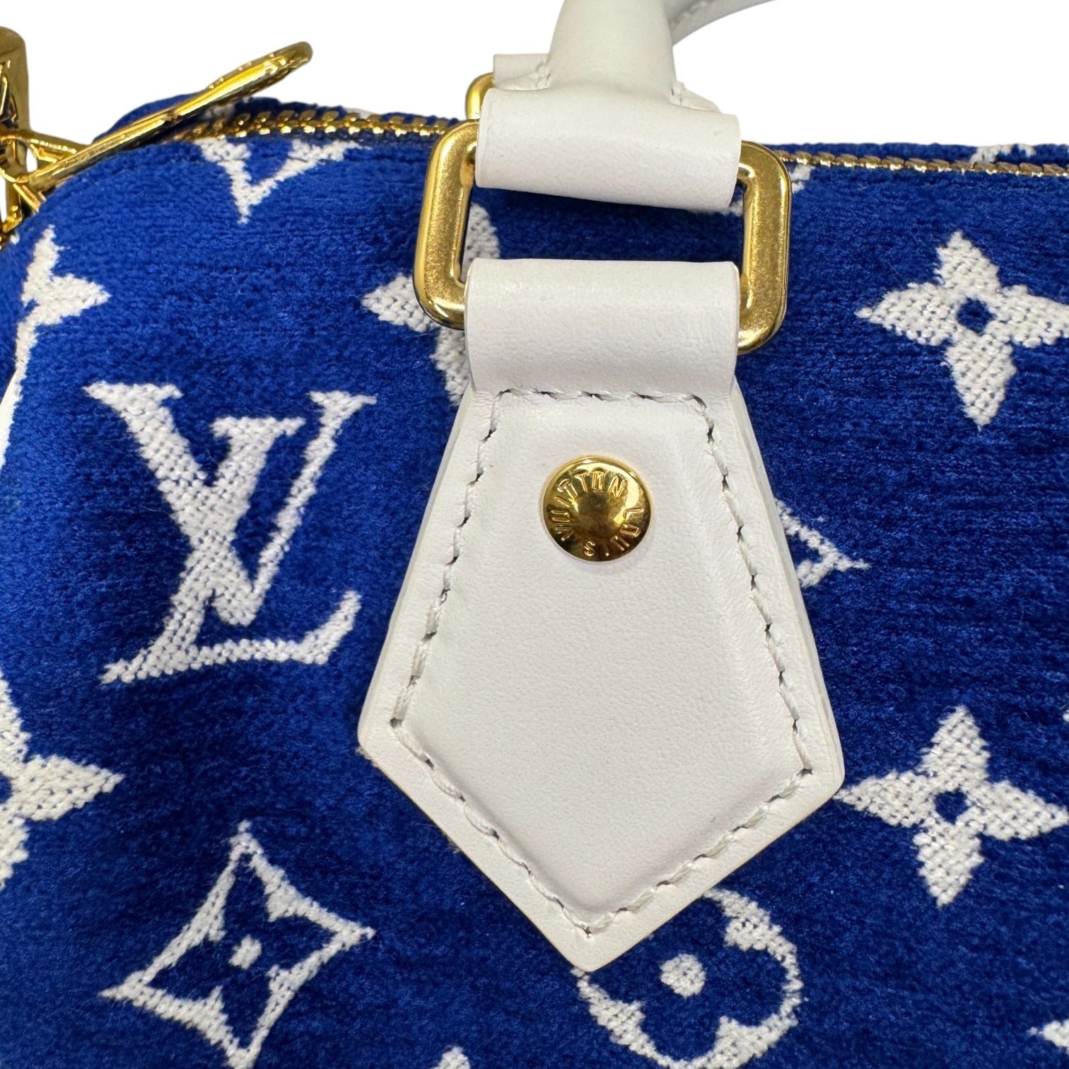 Close-up of a blue handbag with white monogram pattern and gold accents.