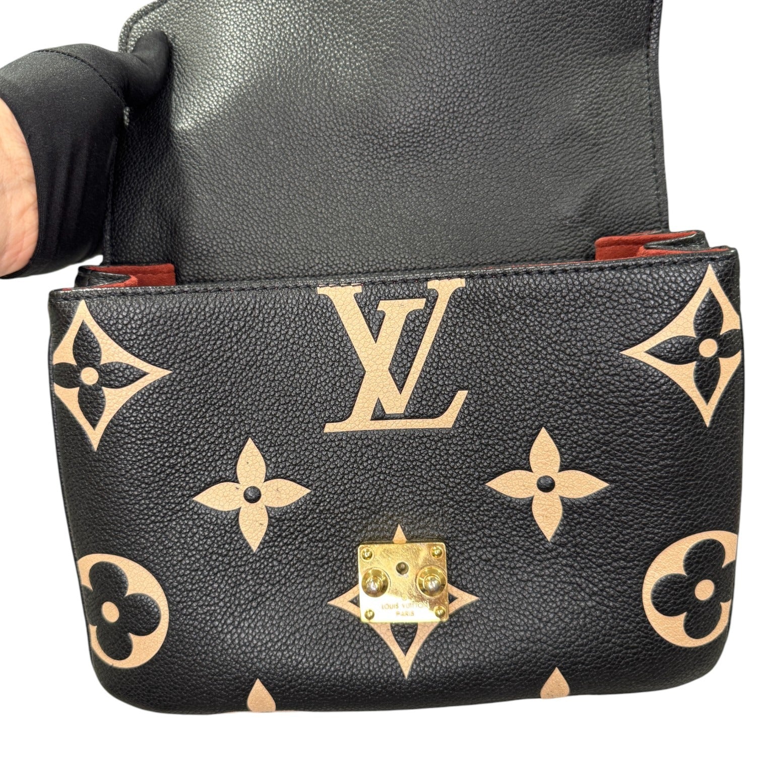 Black leather pouch with gold monogram pattern held by a person wearing black gloves.