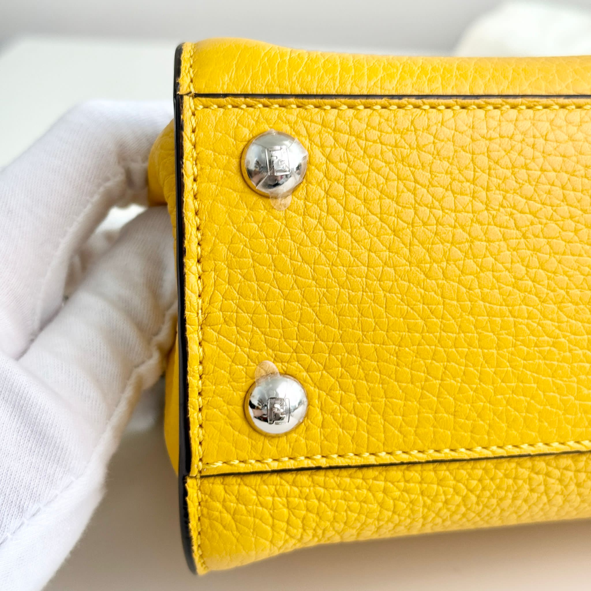 Yellow leather wallet with silver buttons held by a white gloved hand.