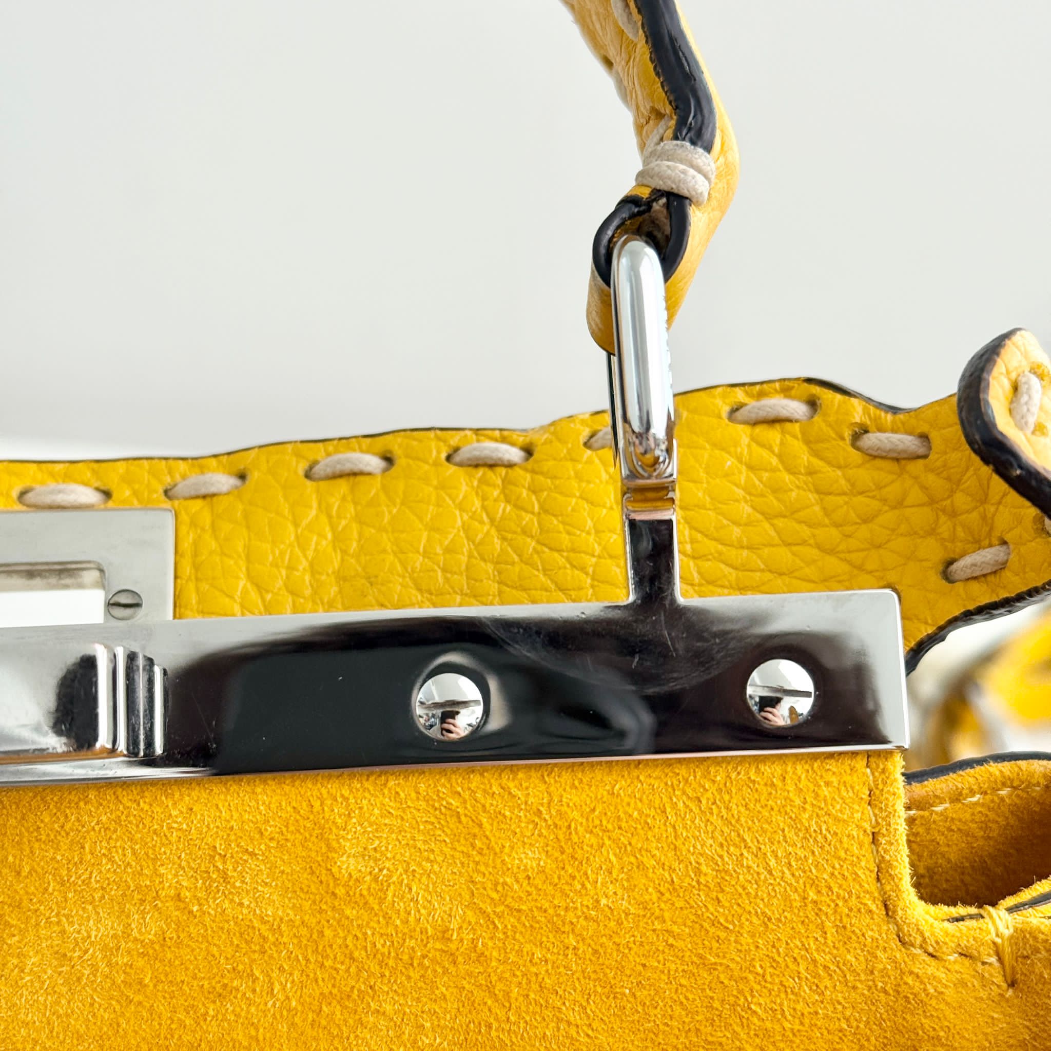 Close-up of a yellow leather product with metal hardware on a light gray background