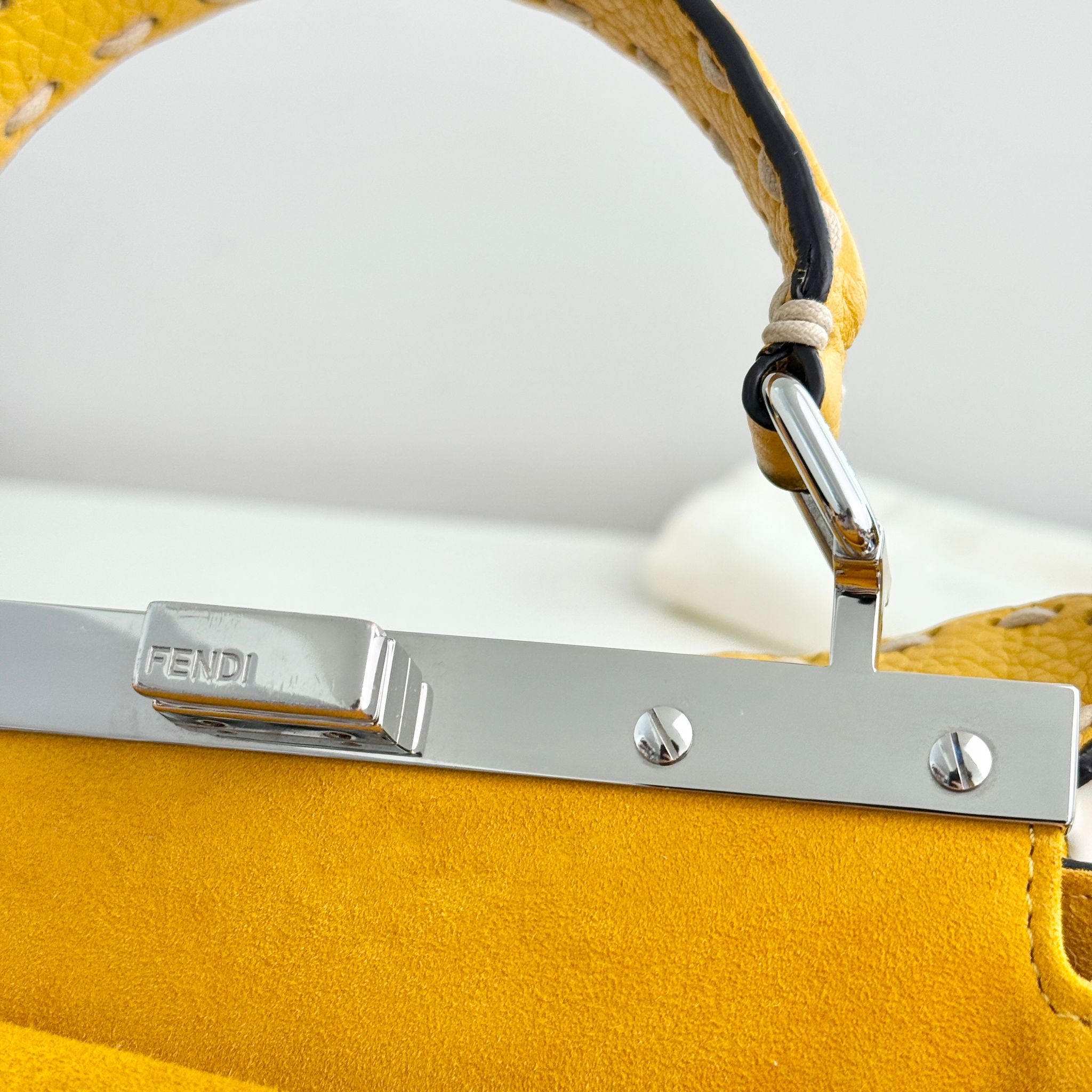 Close-up of a yellow handbag with a silver Fendi clasp on a white background