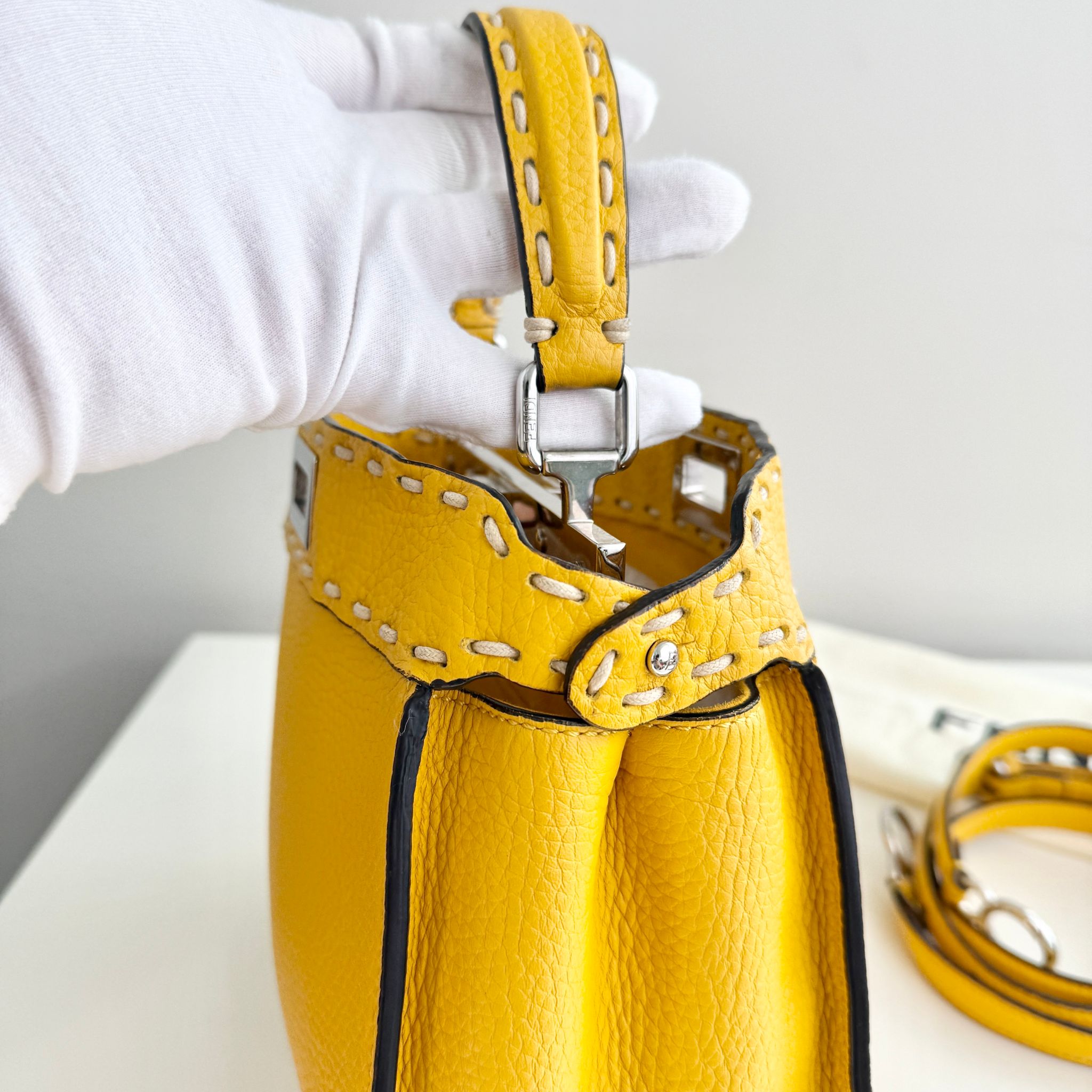 Yellow leather handbag with studded details held by a gloved hand on a white background
