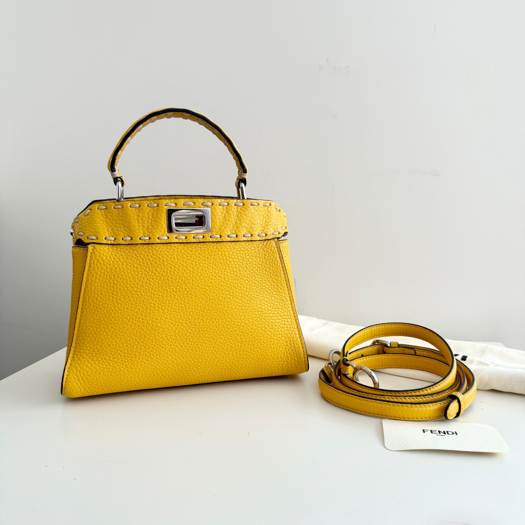 Yellow handbag with matching strap on a white surface