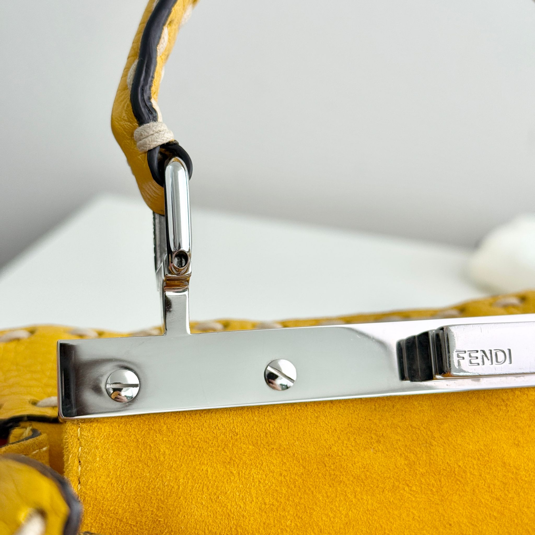 Close-up of a yellow Fendi handbag with a silver clasp on a light gray background