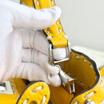 将图片加载到图库查看器，Yellow leather product with silver buckle held by a gloved hand against a neutral background
