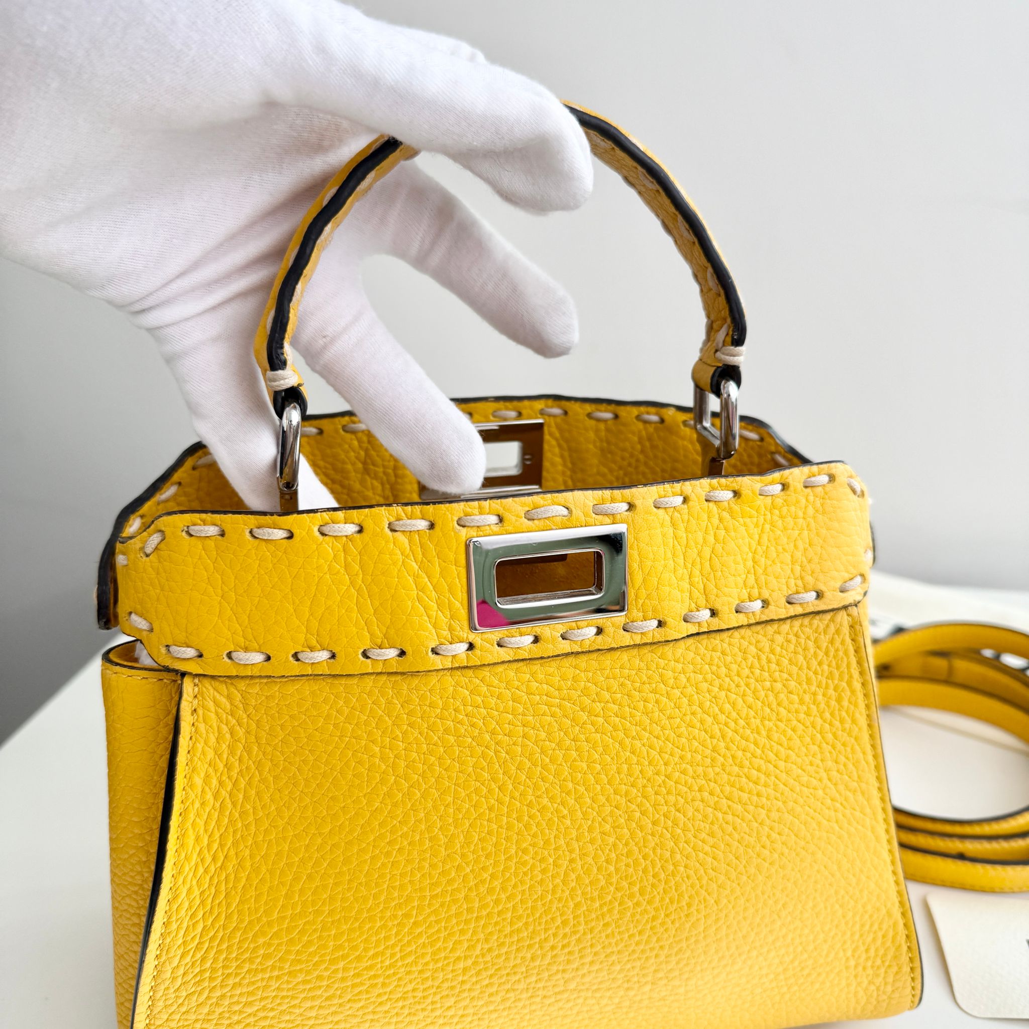 Yellow handbag with a white glove holding it against a neutral background